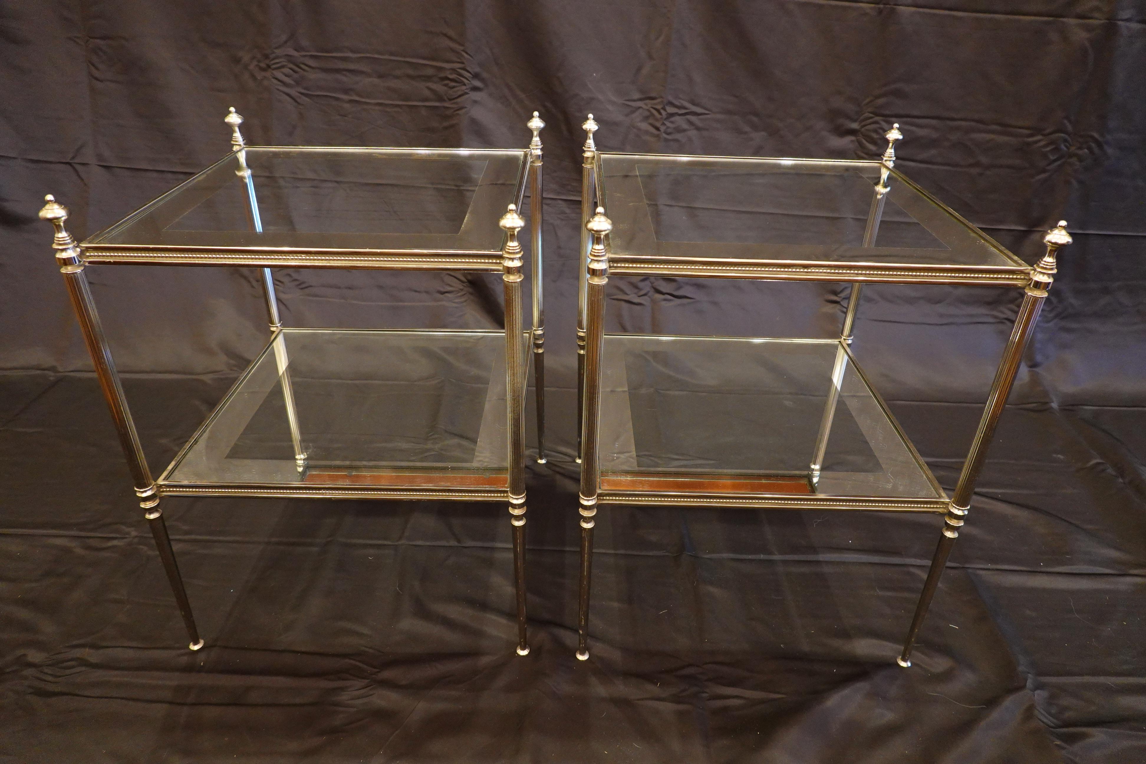 Elegant pair of French silver-bronze two-tiered side tables with glass tops. The rails are decorated with pearl beading, and the legs are fluted in the middle section, tapering to the feet and surmounted with finials. The glass tops are silvered