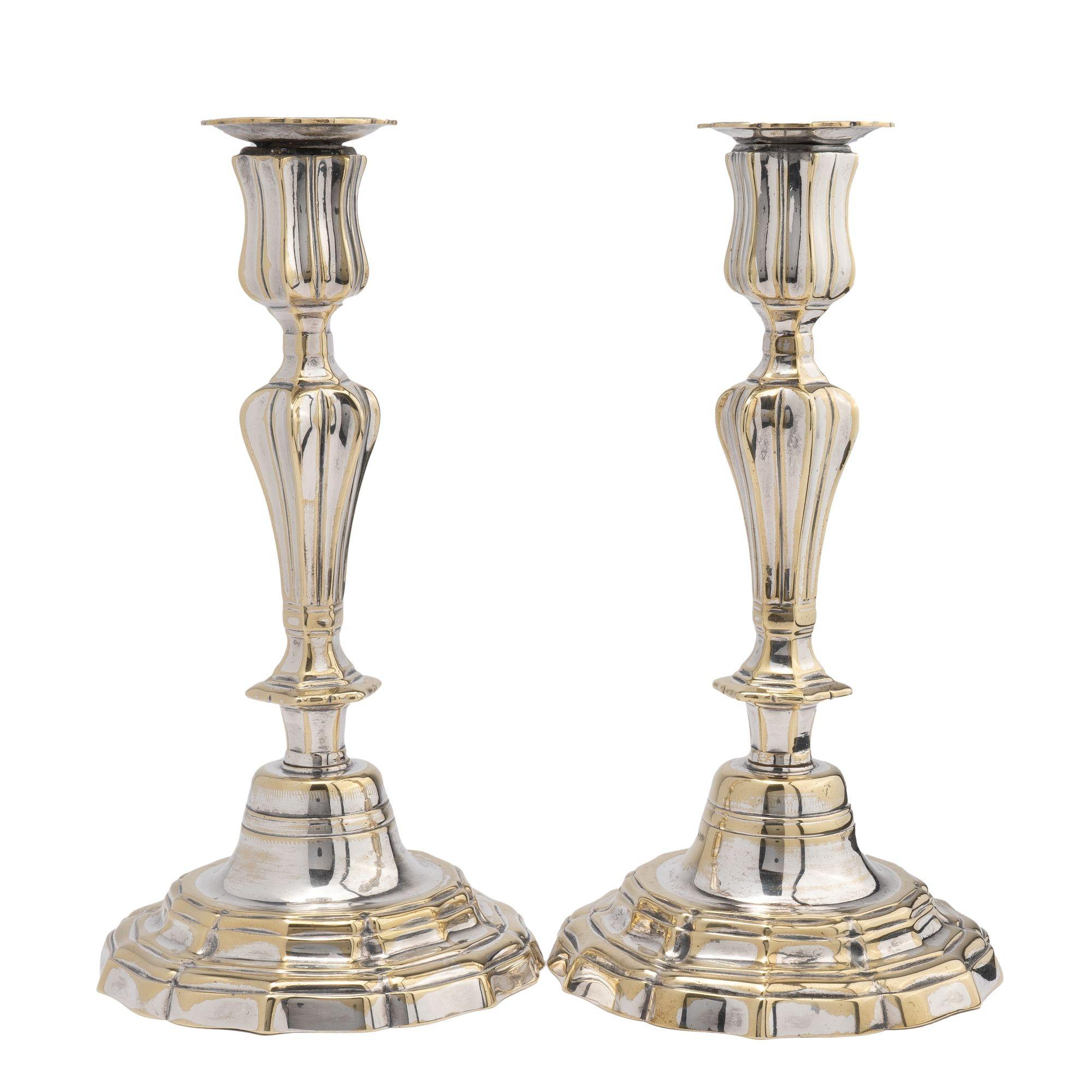 Pair of cast brass and silver plated candlesticks with fluted base and shaft. The candle cup is fitted with a bobeshe in a conforming profile. The stepped, scolloped base and candle shaft are joined by a threaded construction. The exuberance of the