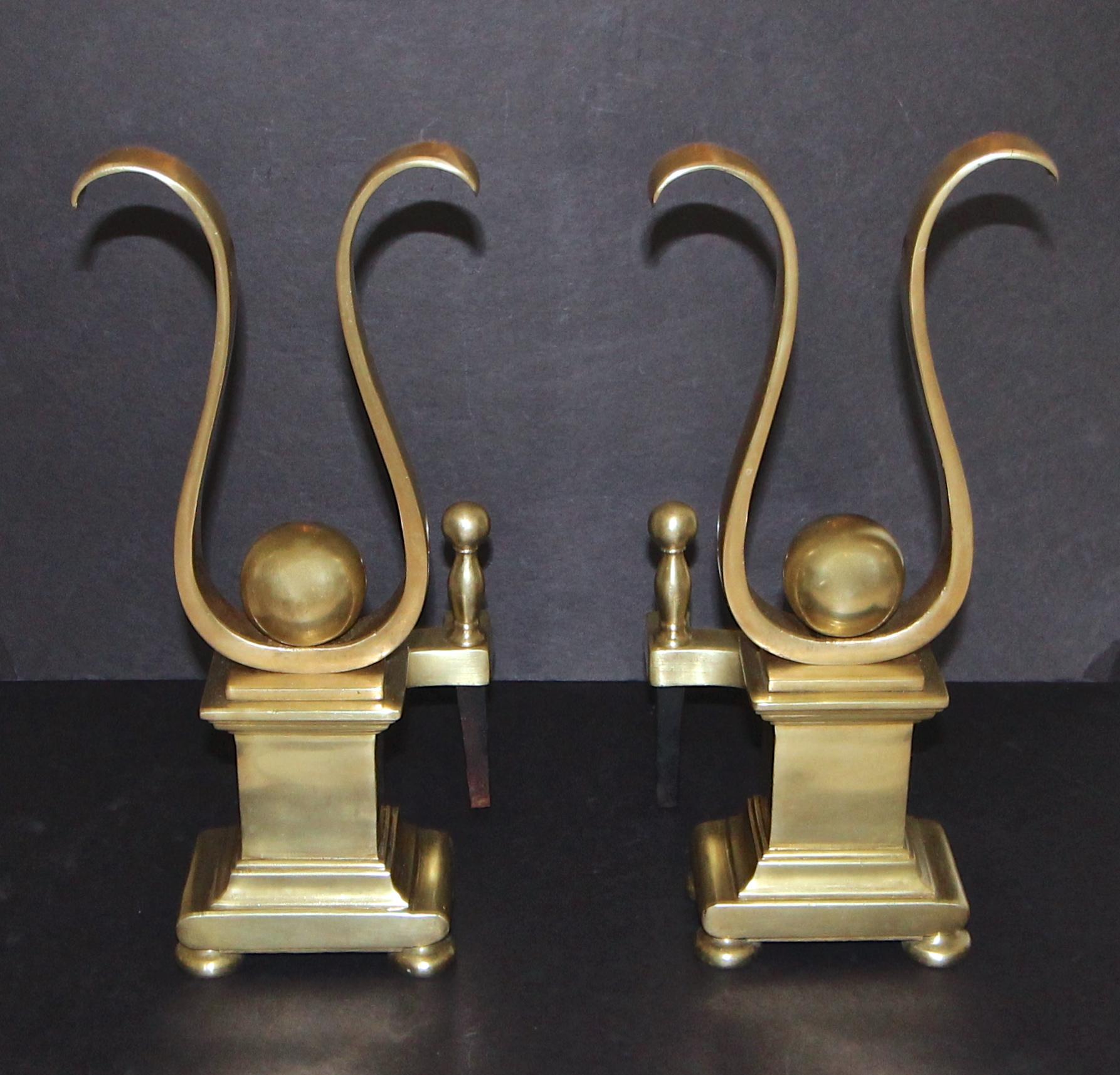 Pair of heavy solid brass lyre shape motif andirons. A stylized version of a Classic silhouette that can blend with both traditional and eclectic interiors.