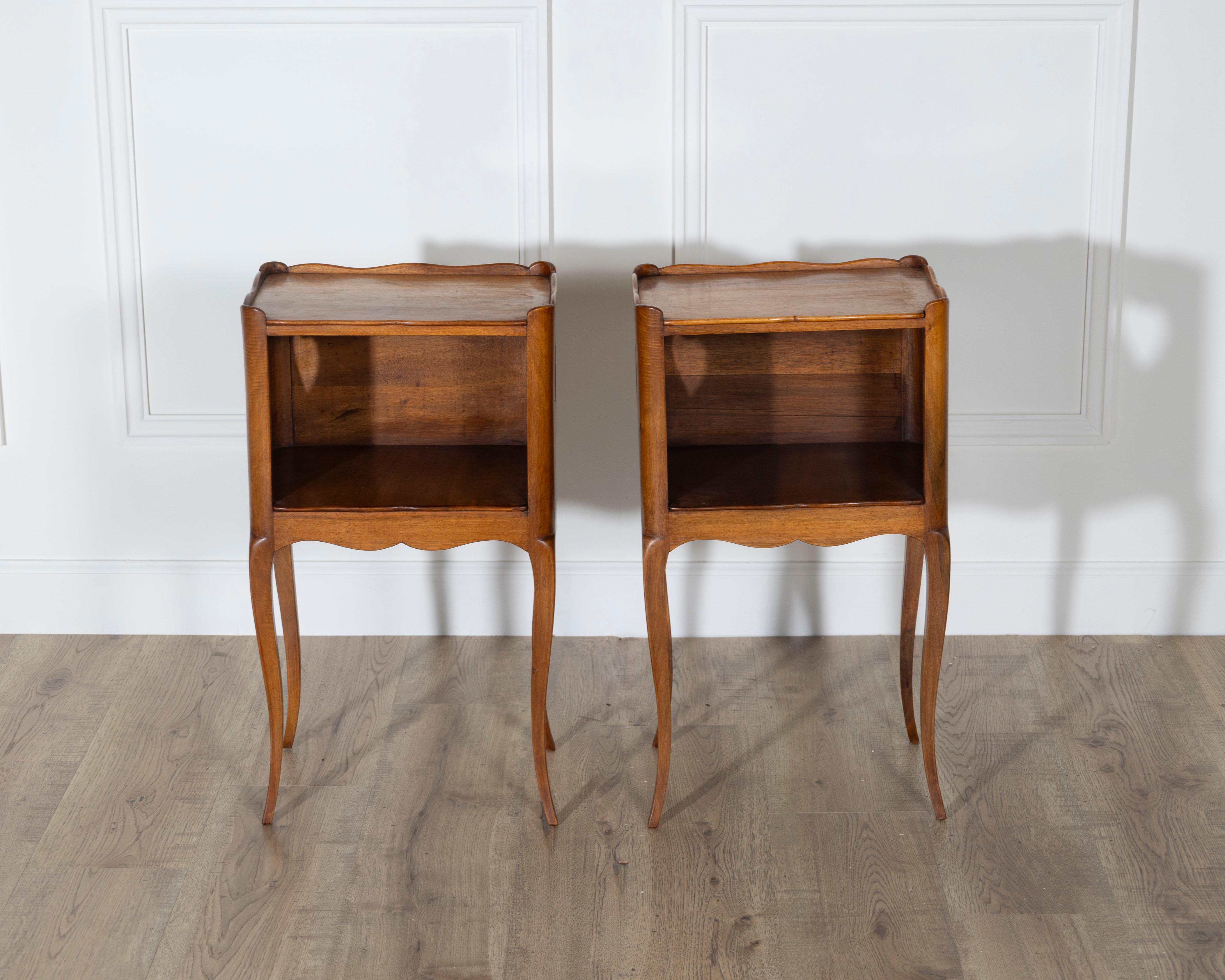 Charmante paire de tables de chevet françaises du XXe siècle, fabriquées en noyer massif et finies avec une cire traditionnelle qui met en valeur le grain naturel et chaud du bois. Chaque table comporte une niche de rangement ouverte, idéale pour