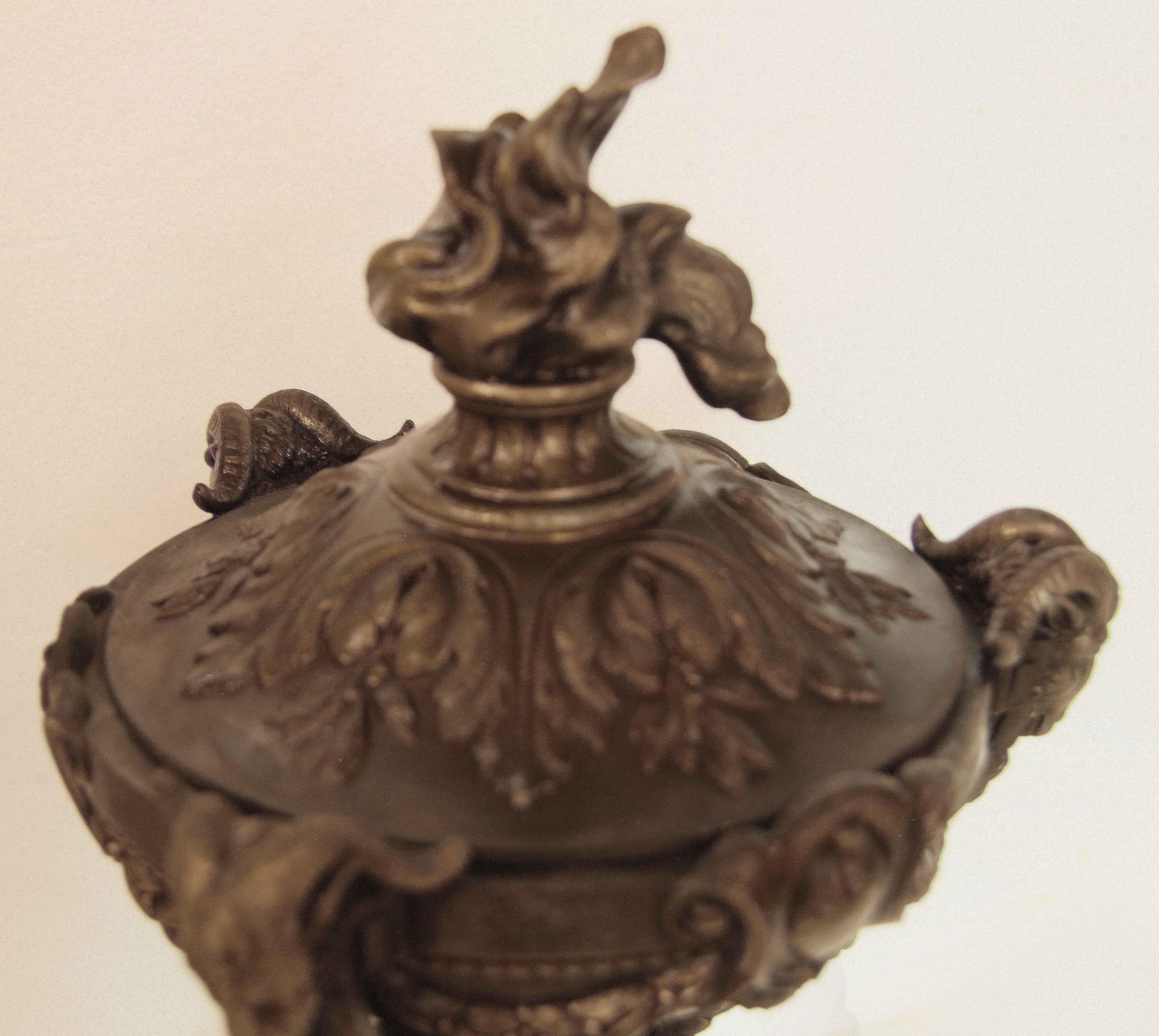Pair of spelter urns,  the lid has a large flame finial with acanthus and foliate surrounding the perimeter below. Inside is a removable brass liner.  A round reeded base with central raised rosette supports three ''legs'' decorated with acanthus