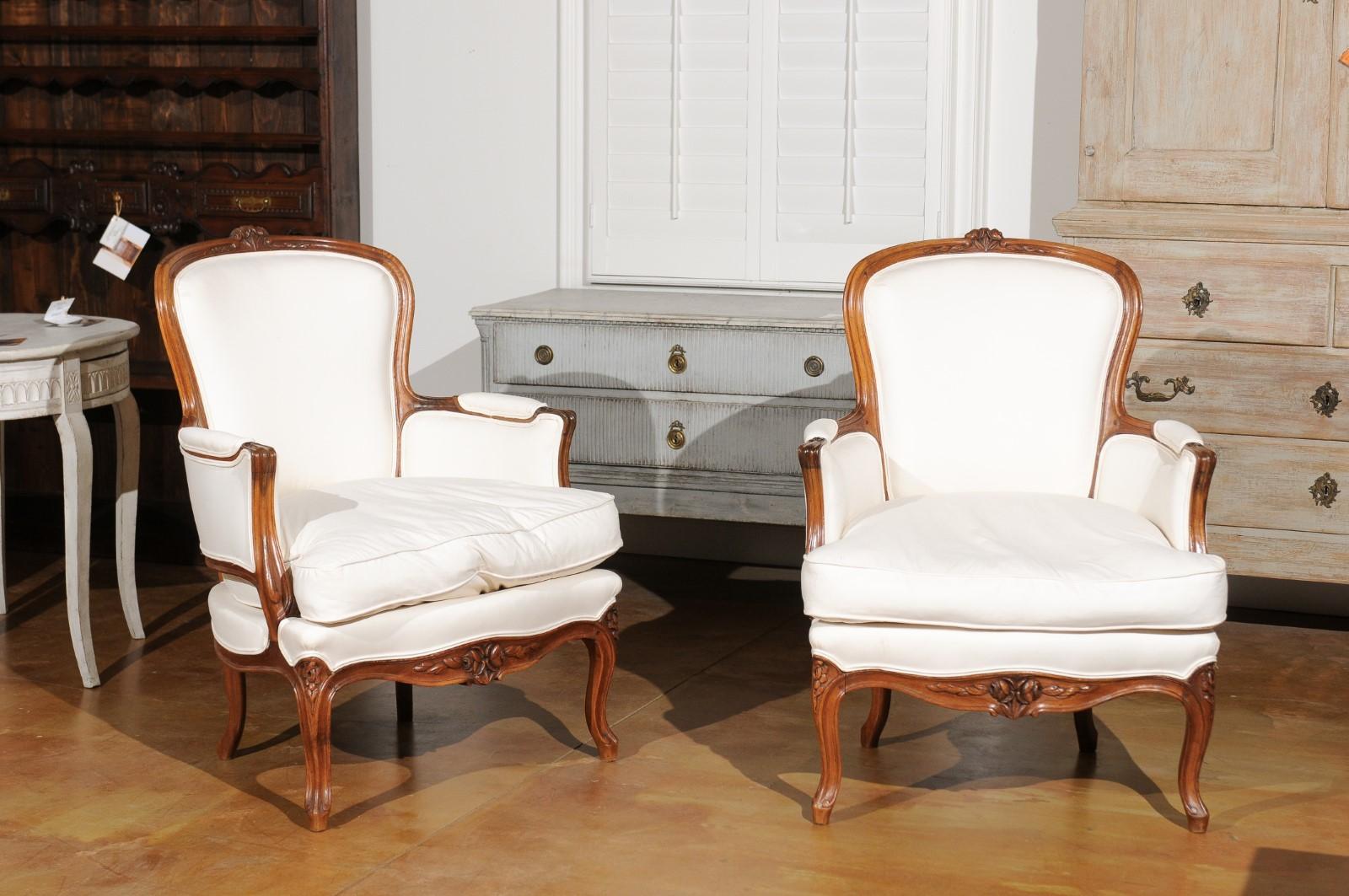 A pair of French Louis XV style walnut armchairs from the late 19th century, stamped and upholstered. Born in France during the later years of the 19th century, this pair of walnut armchairs presents the stylistic characteristics of the Louis XV