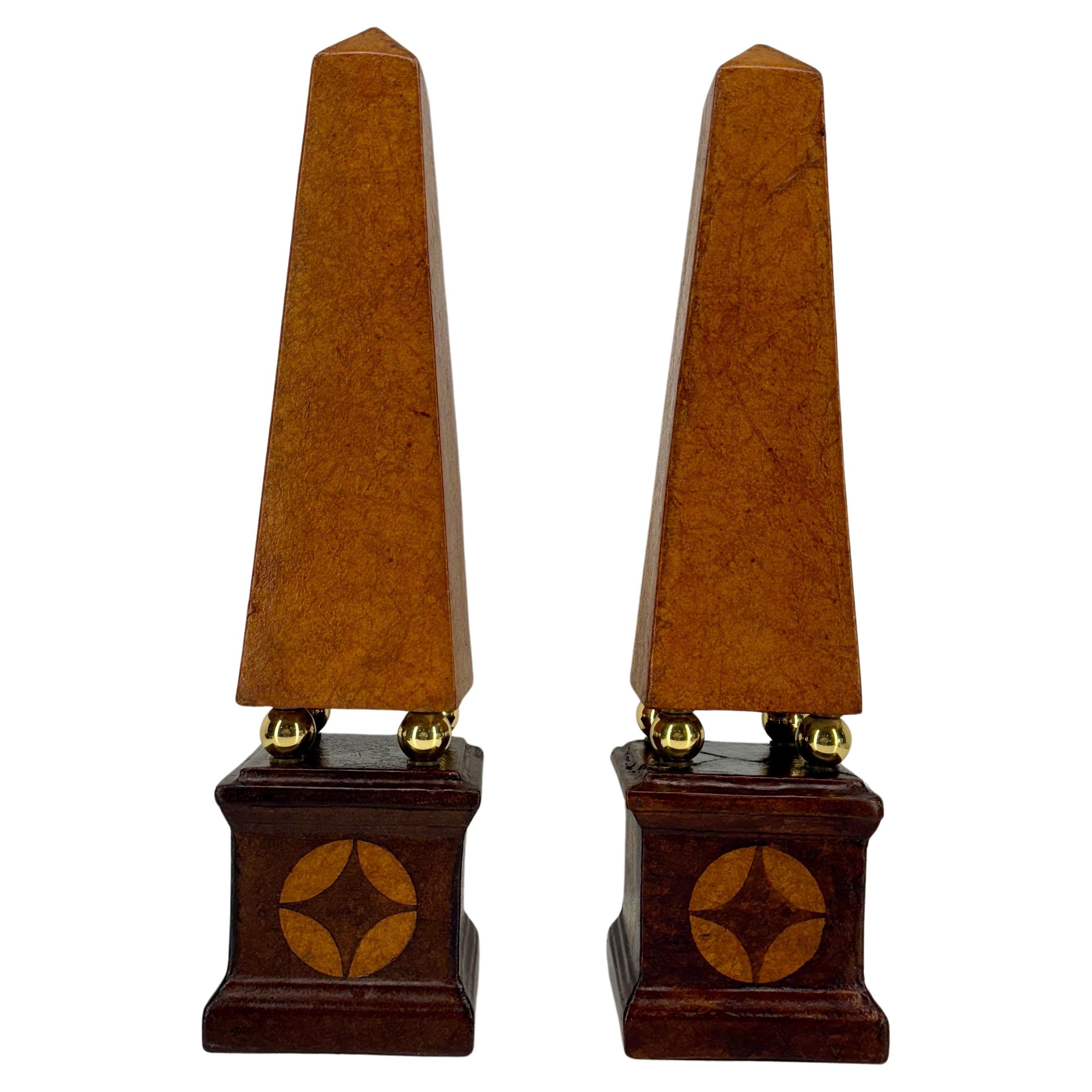 A fantastic pair of ceramic obelisks wrapped in leather from France. 
This delicate ceramic pair are beautifully embossed in classic brown leather with brass balls as detail. This classic set, each standing 21.75