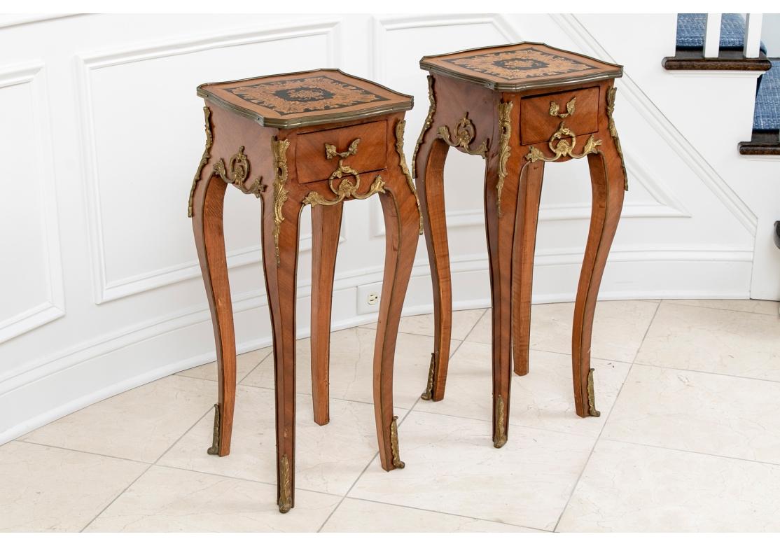 Overall parquetry construction. The shaped tops with canted corners, brass edges and floral marquetry banding on black panels. With a single apron drawer with brass leafy pull. Raised on tall elegant cabriole legs with brass mounts on the tops and