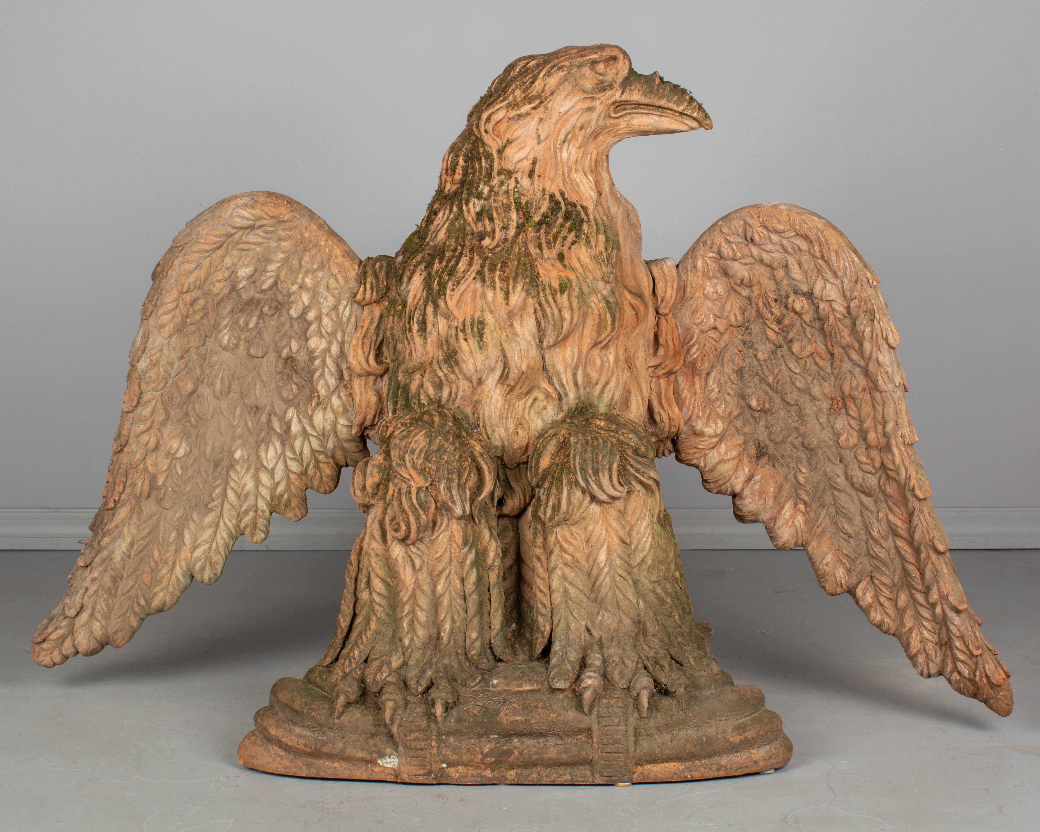 An exceptional pair of early 20th century French terracotta eagle sculptures. A true pair, these regal birds face each other with fierce expressions. They sit perched with impressive talons clutching a low plinth, wings outstretched. Richly detailed