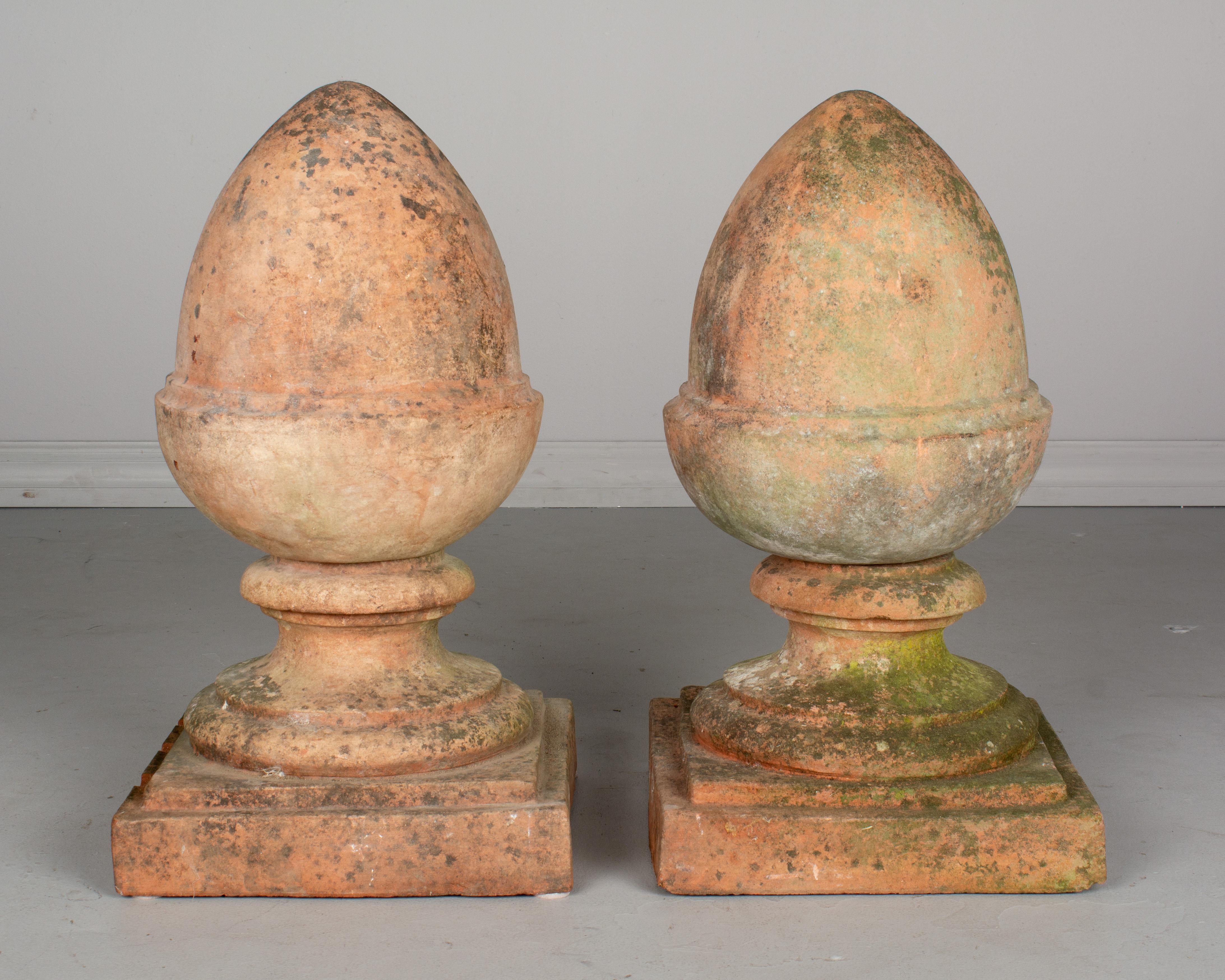 A pair of French terracotta architectural finials with beautiful mossy patina. Perfect for use as ornamental elements in the garden. Each in two parts with the acorn shaped top fitting onto the square base. The Tenon is broken off of one base, so