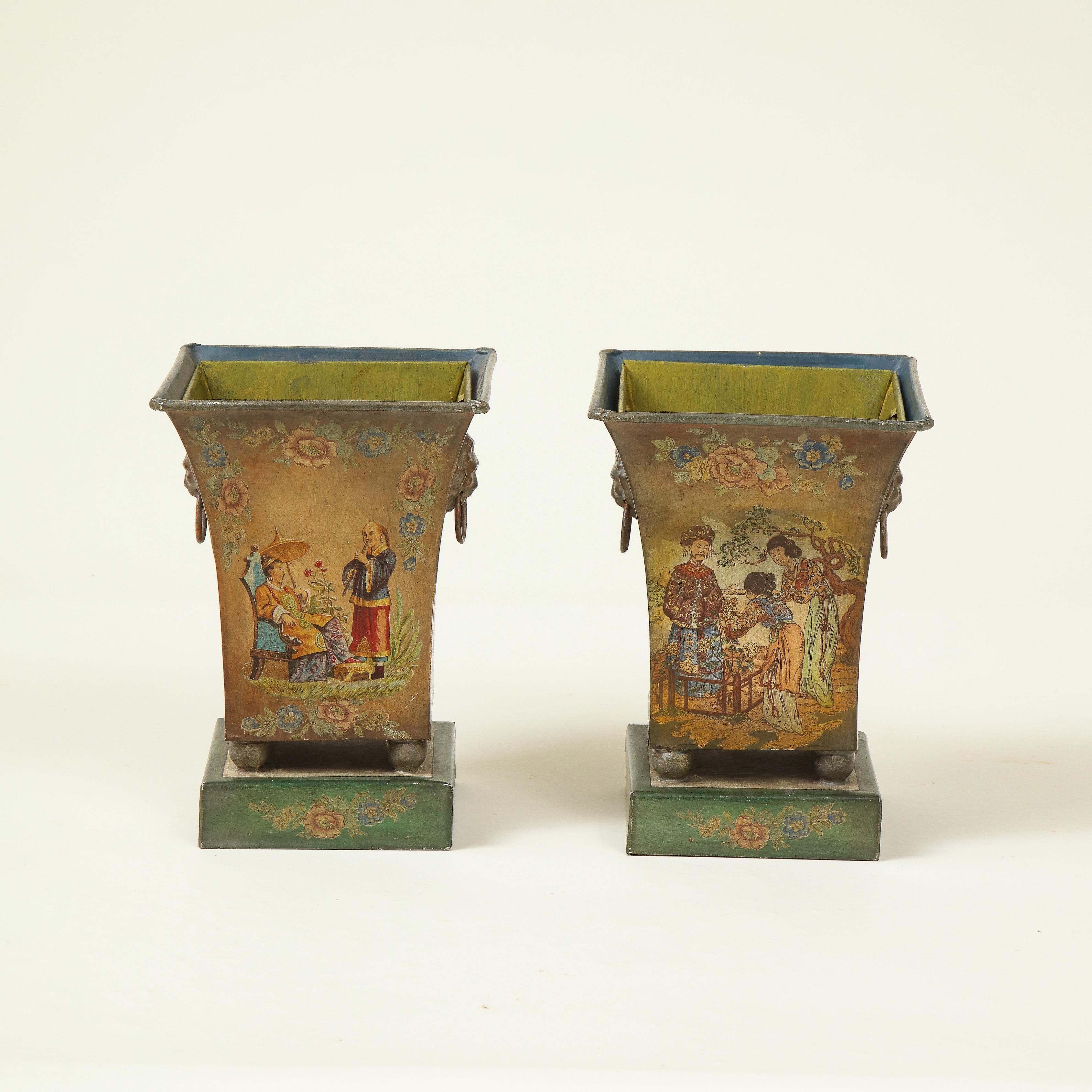 Each of square tapering form, with lion mask ring handles to the sides, on ball feet and a green square plinth base, decorated with Chinese figures in a garden setting and floral garden on an amber ground, with removable liners, signed