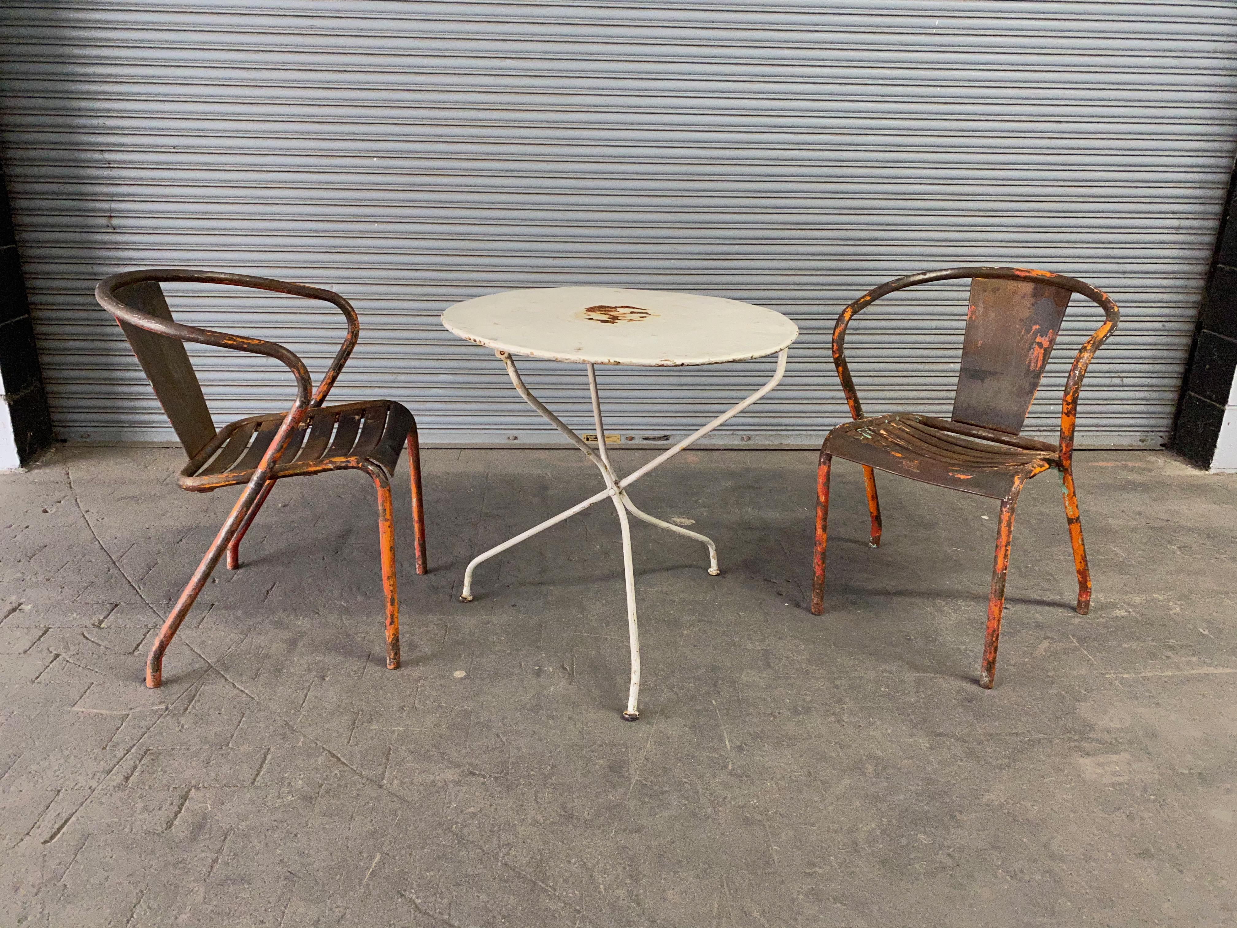 Ein außergewöhnliches Paar französischer Tolix-Sessel aus Metall der 1920er Jahre mit abgenutzter und beschädigter orangefarbener Farbe. Diese charmanten Stühle sind typisch für die Garten- und Bistromöbel in Südfrankreich. Sie vereinen den
