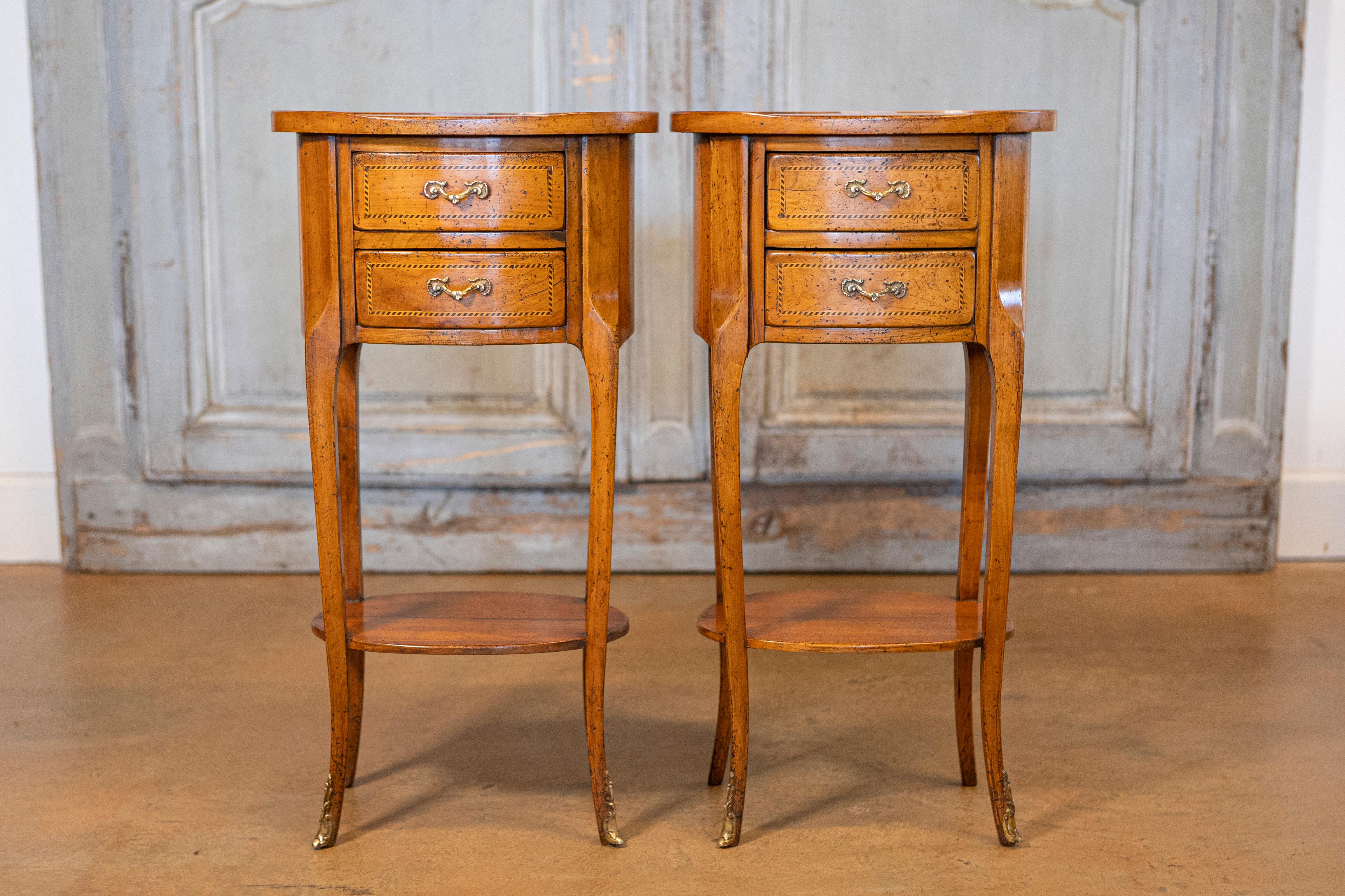 A pair of French Transition style fruitwood oval-shaped bedside tables from the early 20th century with two drawers and marquetry banding. This elegant pair of French Transition style fruitwood oval-shaped bedside tables from the early 20th century