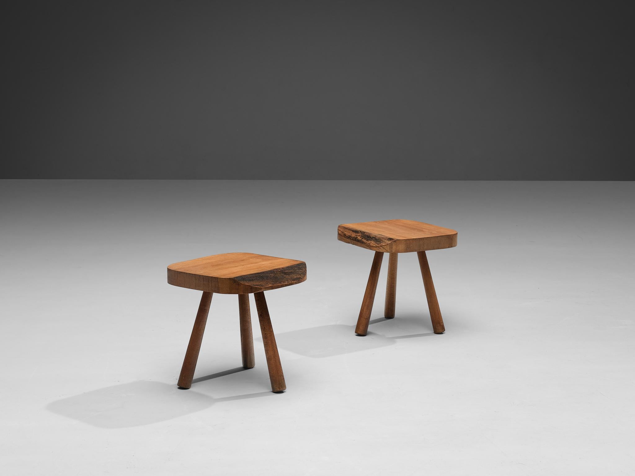 Pair of tripod side tables or small stools, cherry, France, 1960s. 

Rustic pair of French tripod side tables or stools in solid cherry wood. The table top shows some beautiful woodwork. A striking detail is the raw wooden ending on one side of the