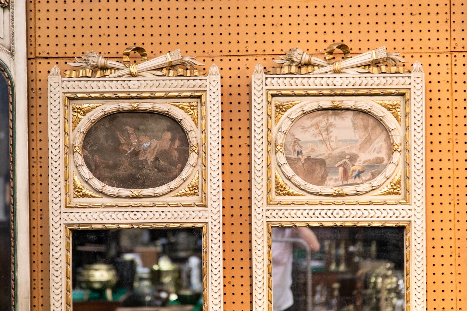 This pair of French trumeau mirrors has repeating carved borders with an oval carved wreath surrounded by four gold carved leaf quarter panels. The upper and lower panels are framed with carved gold repeating ribbon. Inside the oval wreaths are