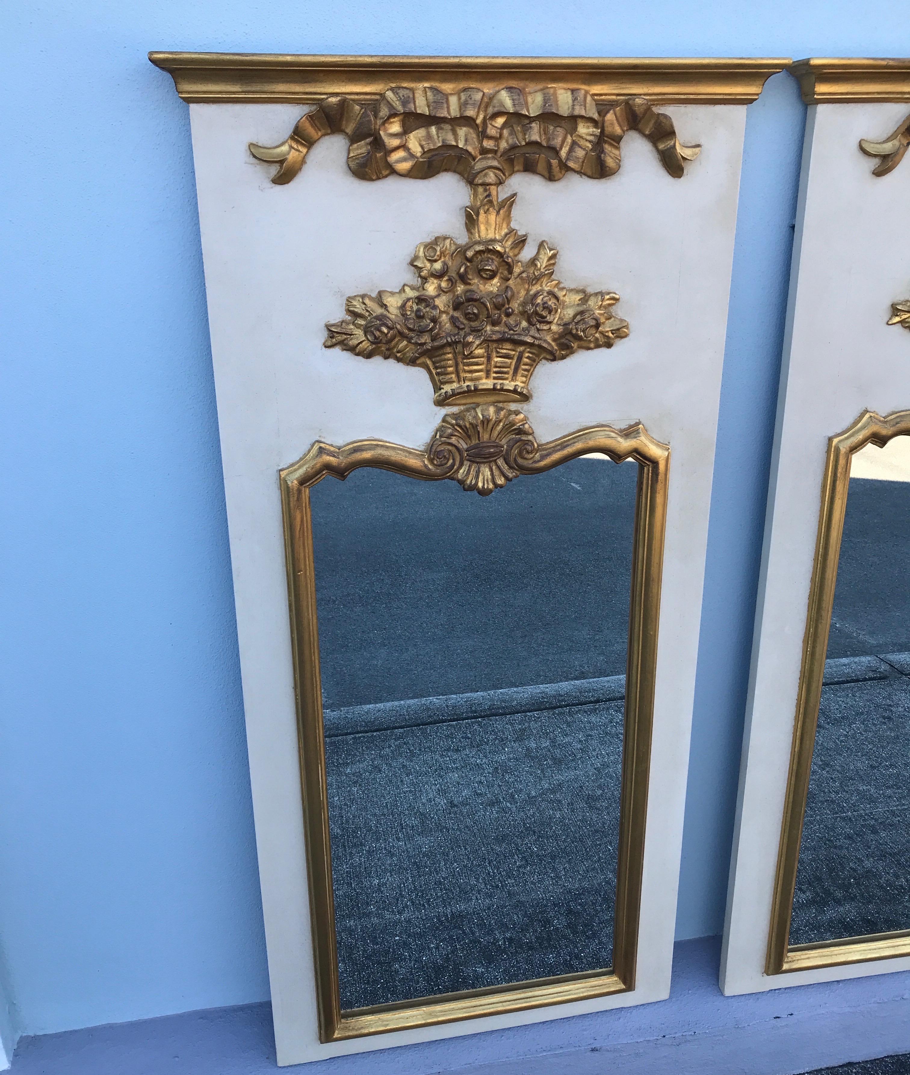Pair of French Trumeau style mirrors in the 18th century design featuring a flower basket motif. Antique white finish with gold leaf.