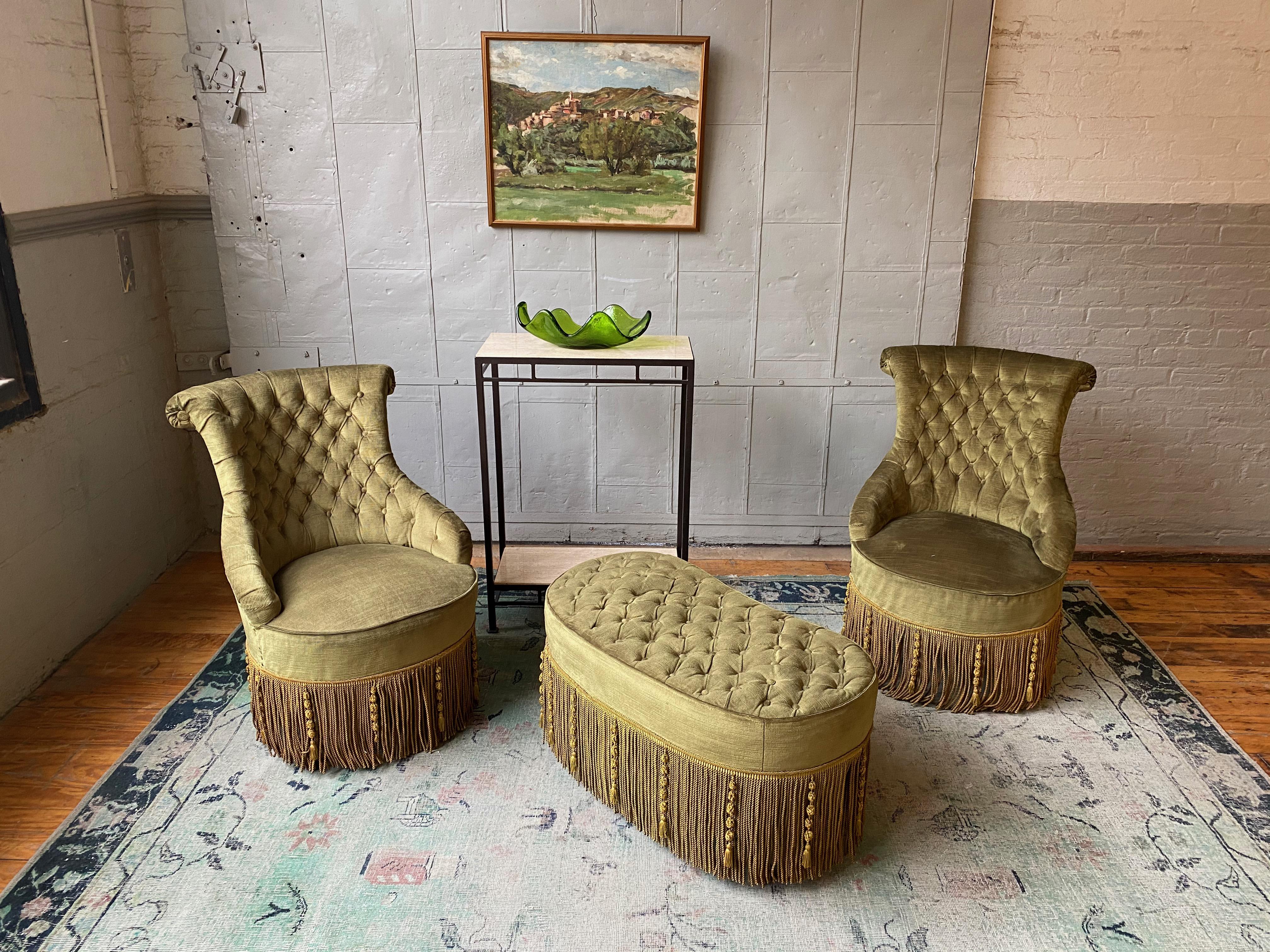Pair of tufted Napoleon III style armchairs in green velvet with contrasting bullion fringe. The pair of chairs are sold with a matching ottoman. 

French late 19th or early 20th century.  The set is in good condition and sold as is.