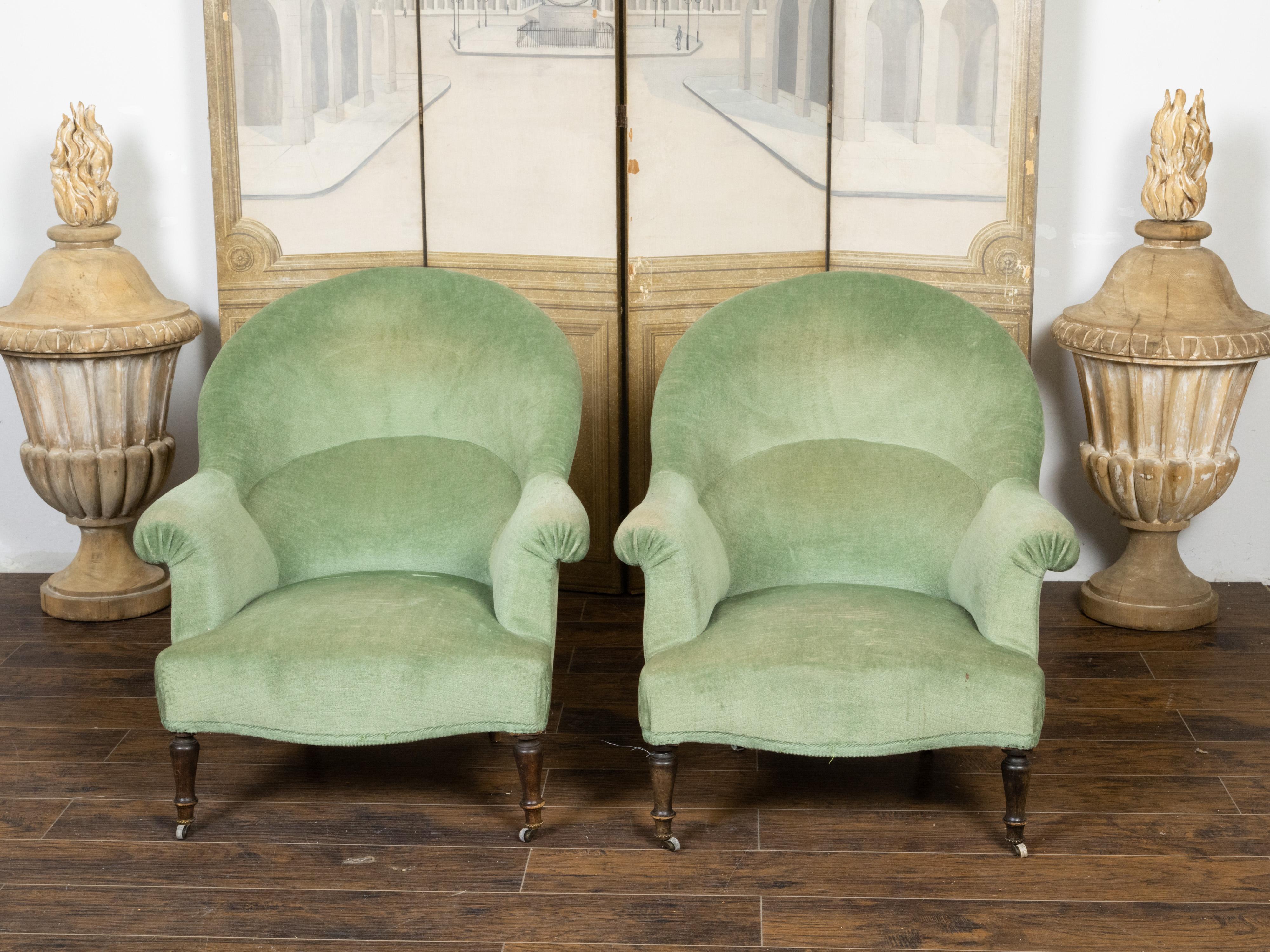 A pair of French turn of the century upholstered bergères armchairs from the early 20th century with old green velvet upholstery, out-scrolling arms and turned legs. Created in France at the turn of the century which saw the transition between the