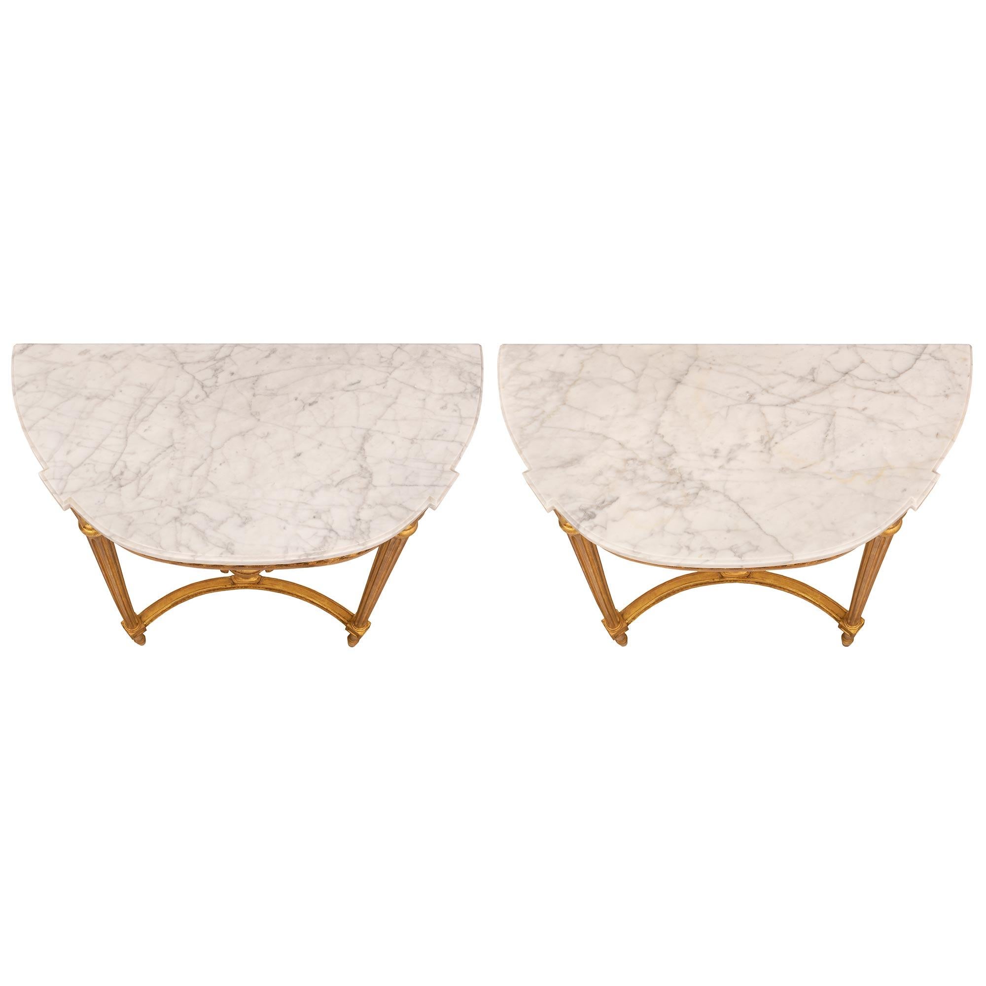 A most elegant pair of French turn of the century Louis XVI st. giltwood and white Carrara marble consoles. Each wall mounted console is raised by lovely slender circular tapered fluted legs with fine topie shaped feet. Above each foot are block
