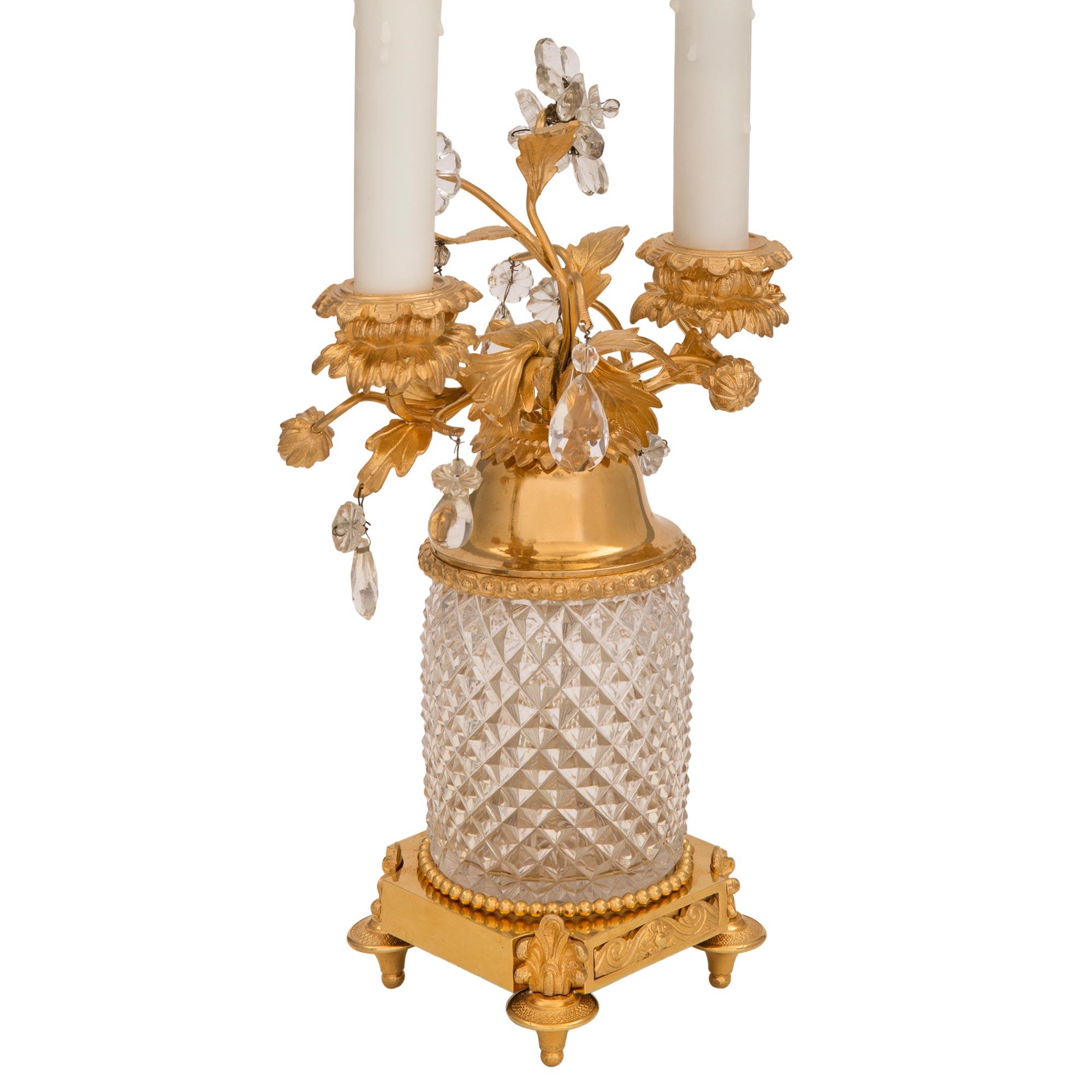 Une paire exceptionnelle de lampes de style Louis XVI du début du siècle, en bronze doré et cristal. Chaque lampe à deux bras est surélevée par une base carrée avec de fins pieds en forme de topie ornés de beaux éléments de palmettes centrant une