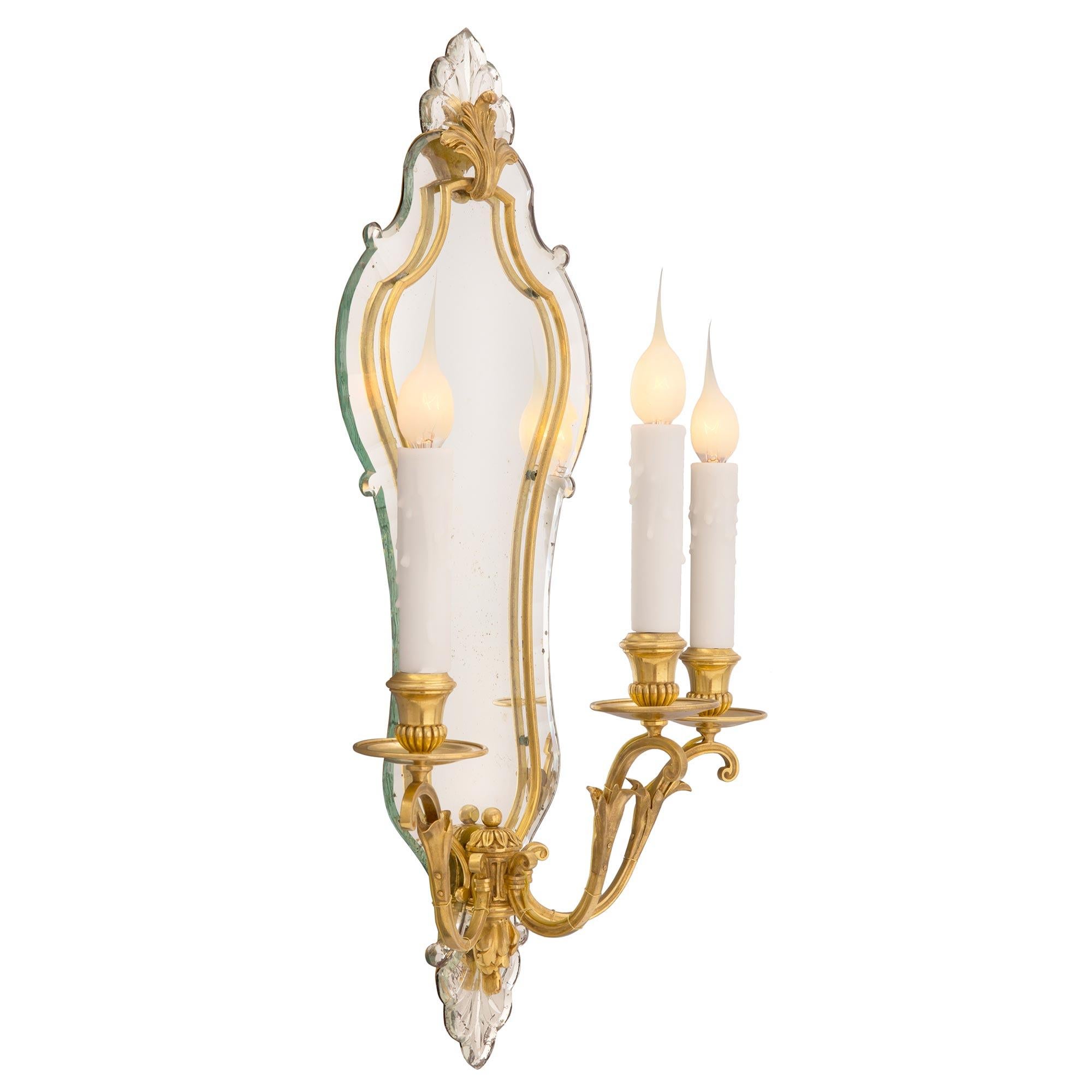 An exceptional and extremely decorative pair of French turn-of-the-century Venetian st. ormolu and mirrored sconces, likely by Maison Bagues. Each three arm sconce displays a stunning scalloped shaped mirrored backplate with impressive wonderfully