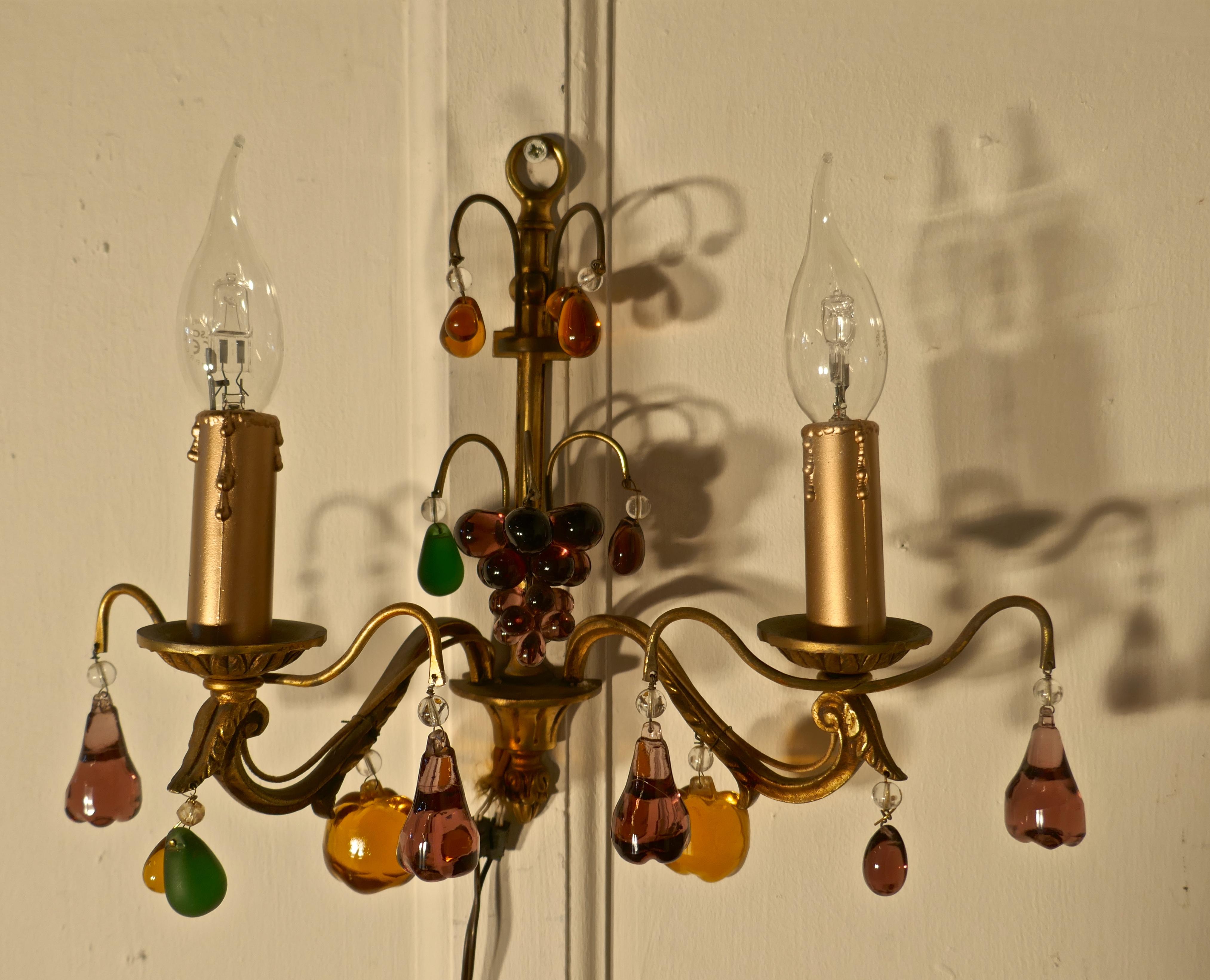 Pair of French twin wall lights hung with crystal fruit.

These are a very pretty pair of double wall lights, the gilded brass sconces are hung with coloured crystal pendants in the shape of fruits, amethyst grapes and pears and amber apples 
All