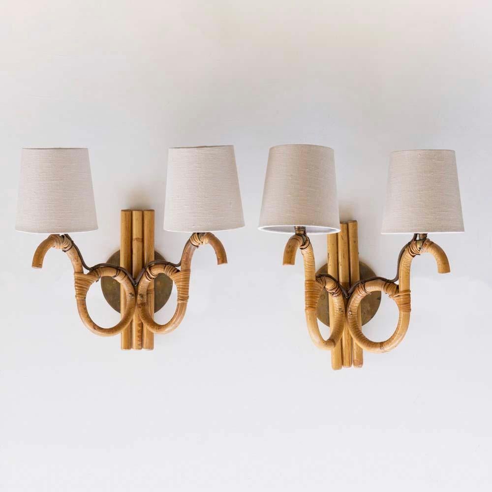 Wonderful pair of rattan sconces from France, 1960s, in the style of Louis Sognot. Two curvy rattan arms with loop detail and wrapped rattan detailing. Newly re-wired with new tapered linen shades. New brass backplates measure 4