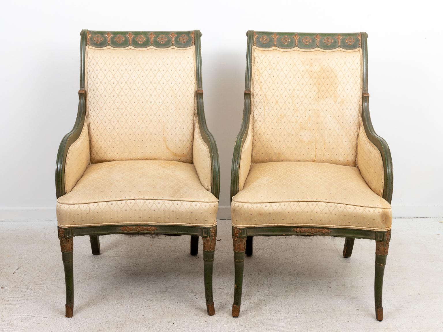 Pair of French Empire style upholstered armchairs carved and painted floral trim on the top of the seat backs and legs. Please note of wear consistent with age including paint loss and finish loss, there is also evidence of staining on the