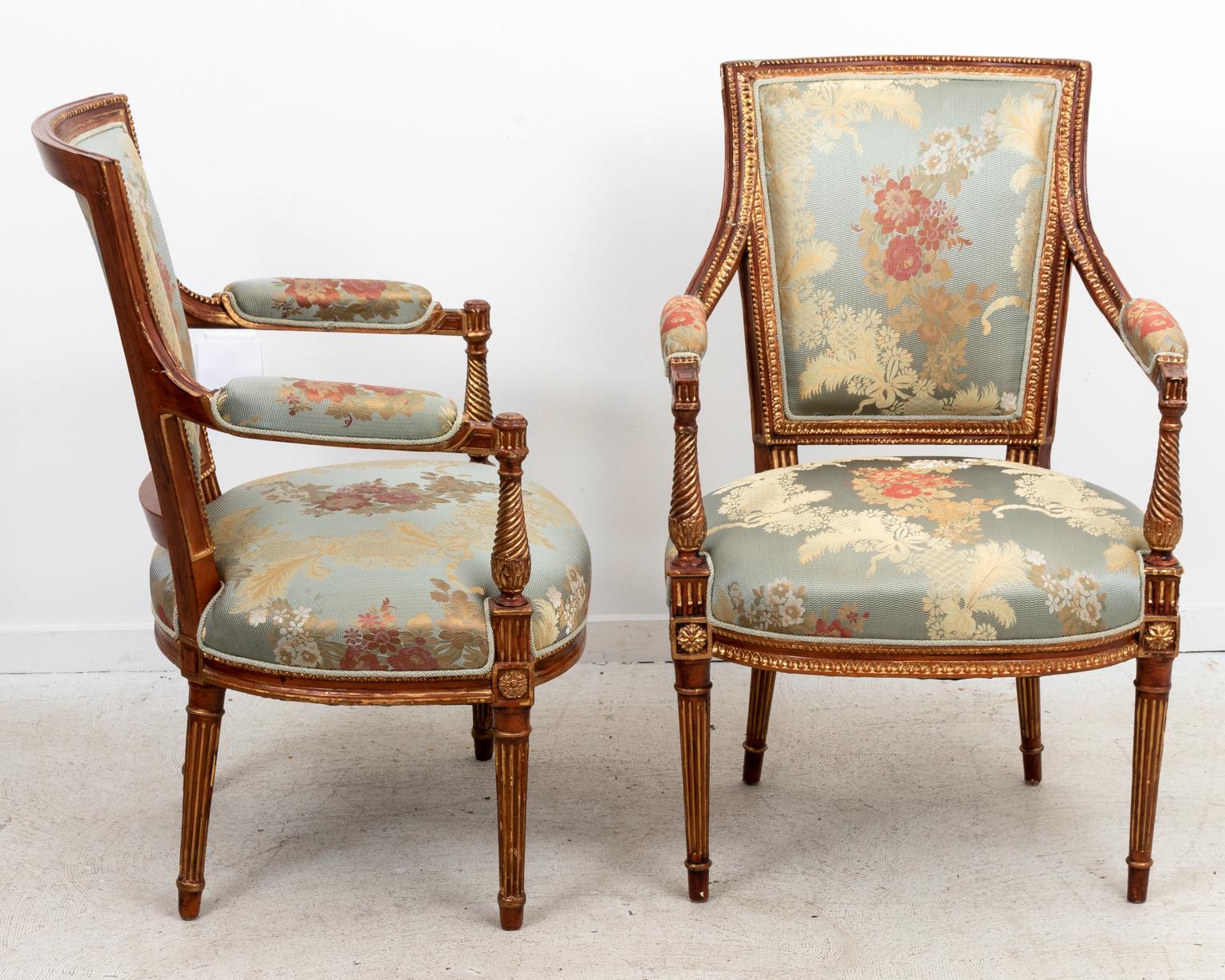 Pair of French upholstered open armchairs with rectangular backs and upholstered armrests. Please note of wear consistent with age including chips, wood loss, and finish loss.