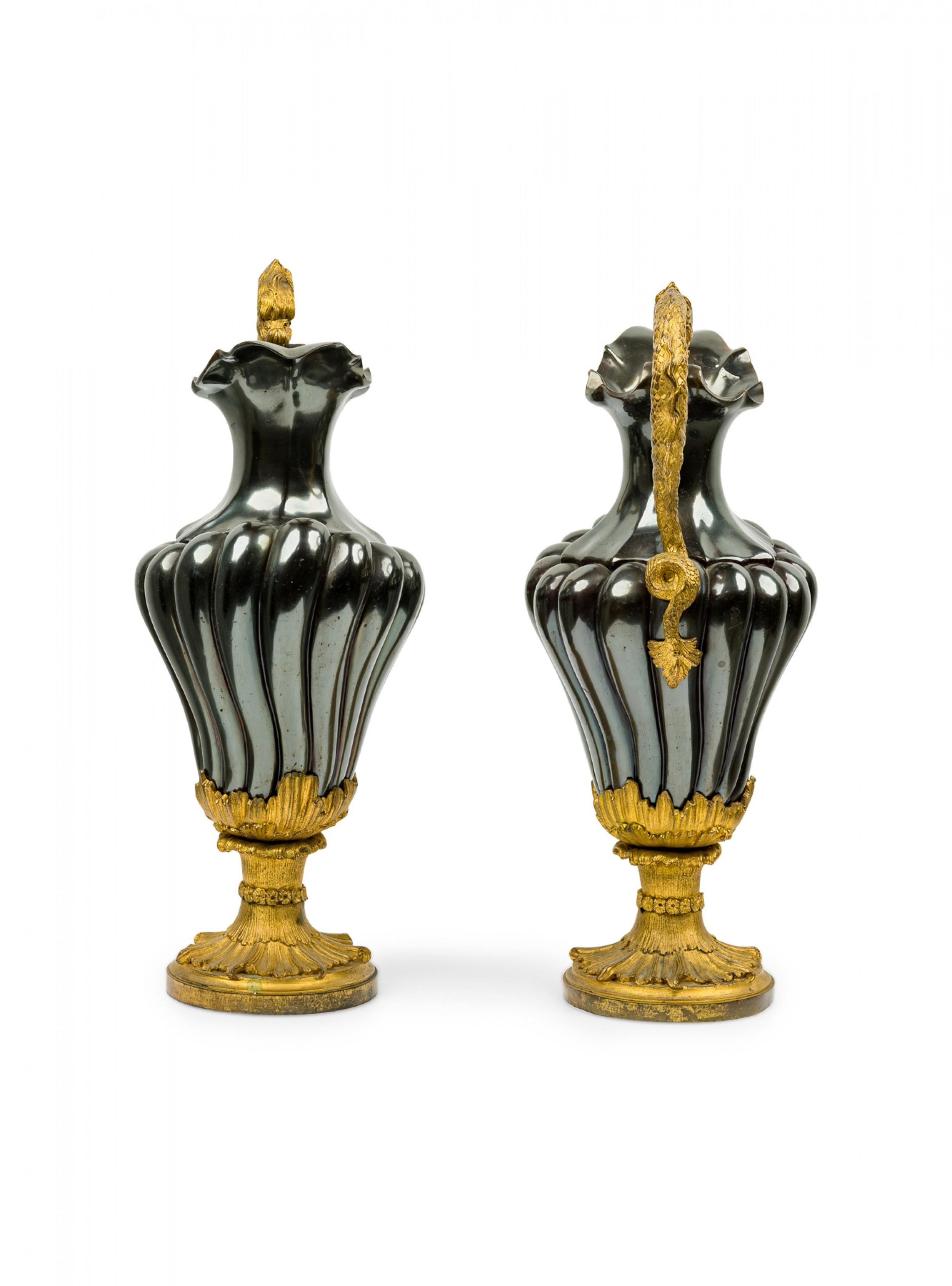 Pair of French Victorian urns / ewers with metallic black enameled fluted bodies and elaborate gilt bronze serpent handles resting on ormolu foliate detailed circular base.