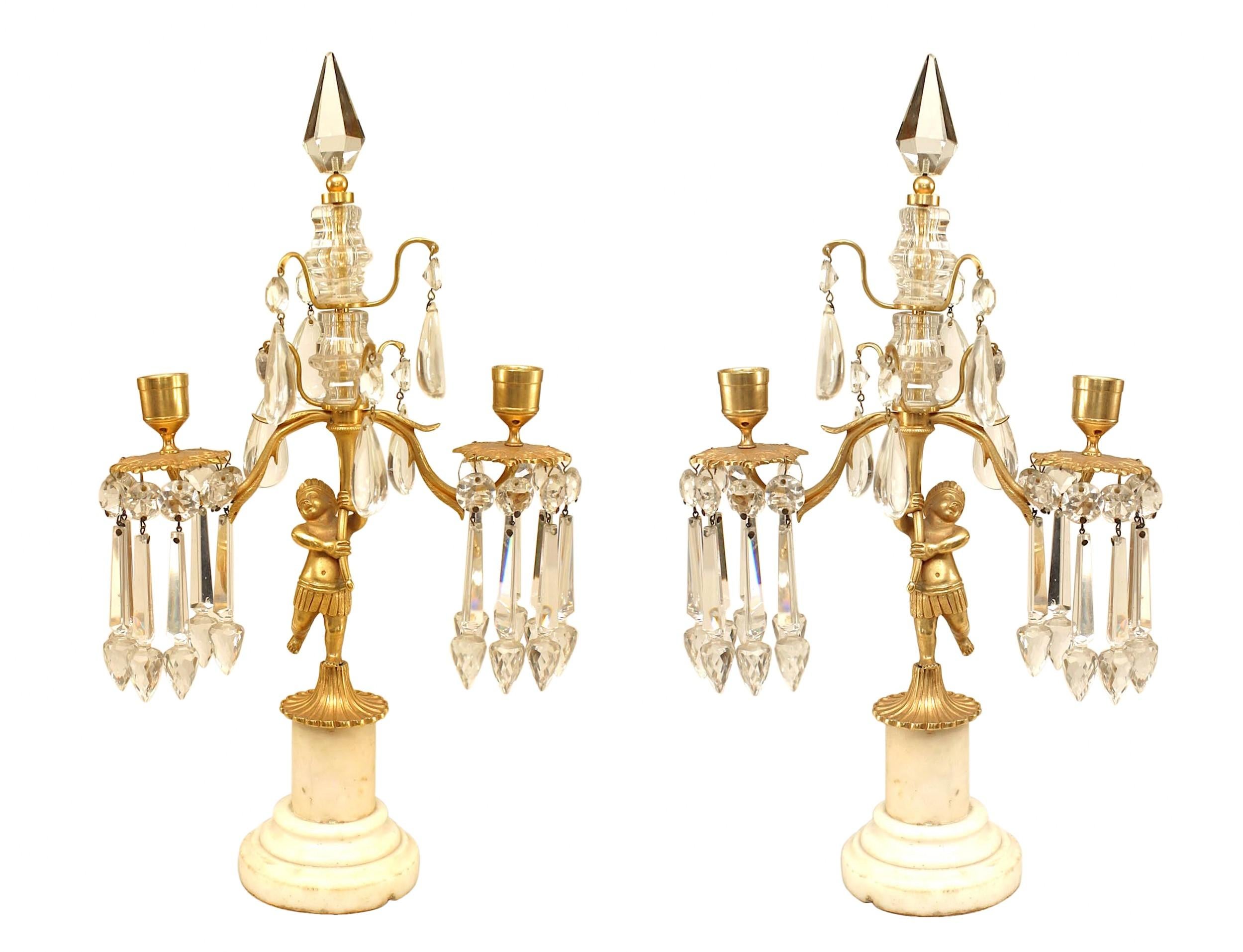 Paire de candélabres victoriens (19e/20e siècle) à 2 lumières en bronze doré tenus par une figure de cupidon avec des gouttes et des prismes en cristal taillé, avec une base en colonne blanche et un sommet en forme de fleuron (PRIX PAR Paire)

Il