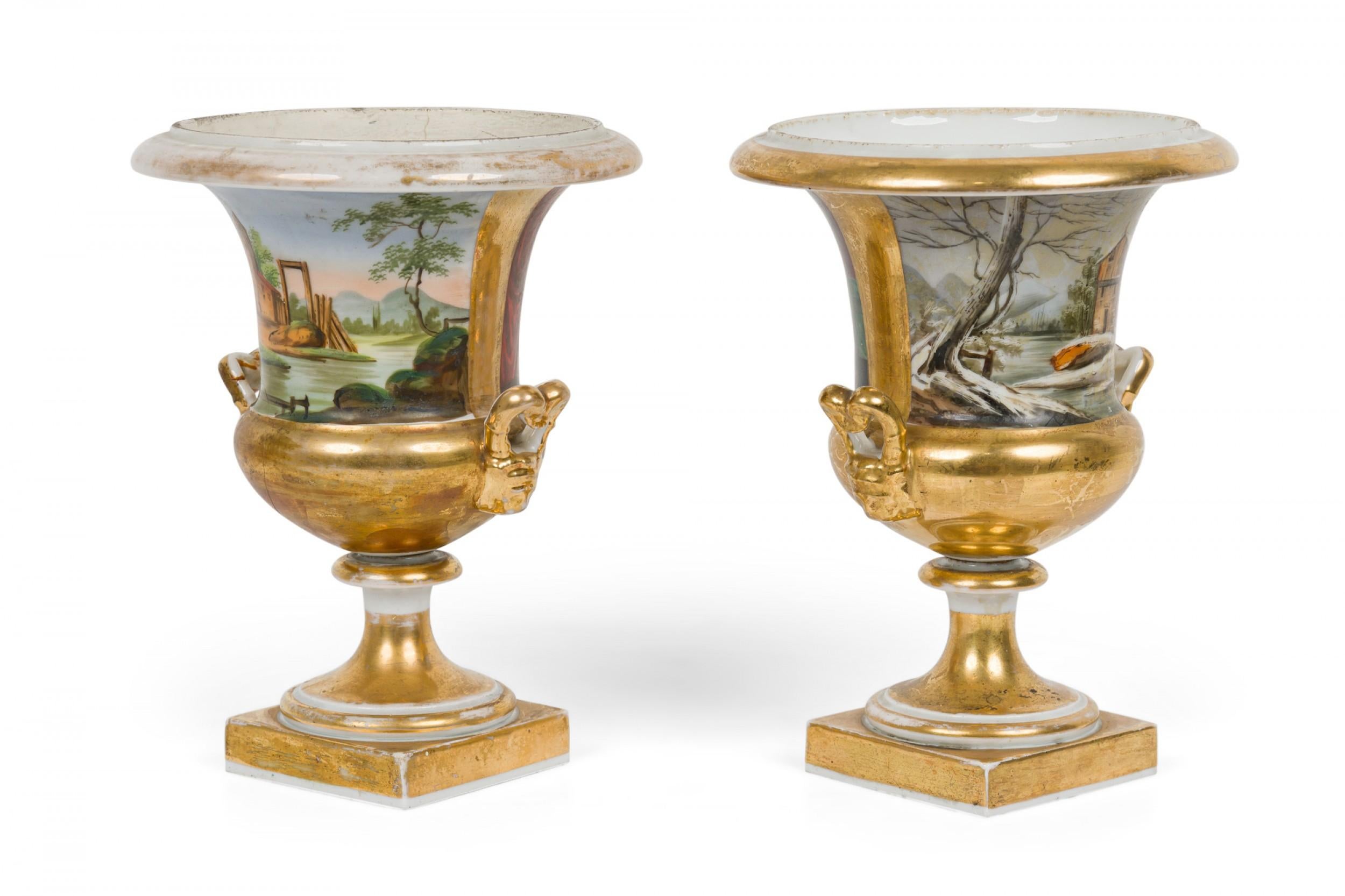 PAIR of French (19th century) Sevre porcelain urns featuring painted pastoral scenes on one side and genre scenes on the reverse, with gilt trim, handles and bases, resting on square porcelain bases. (PRICED AS PAIR).
