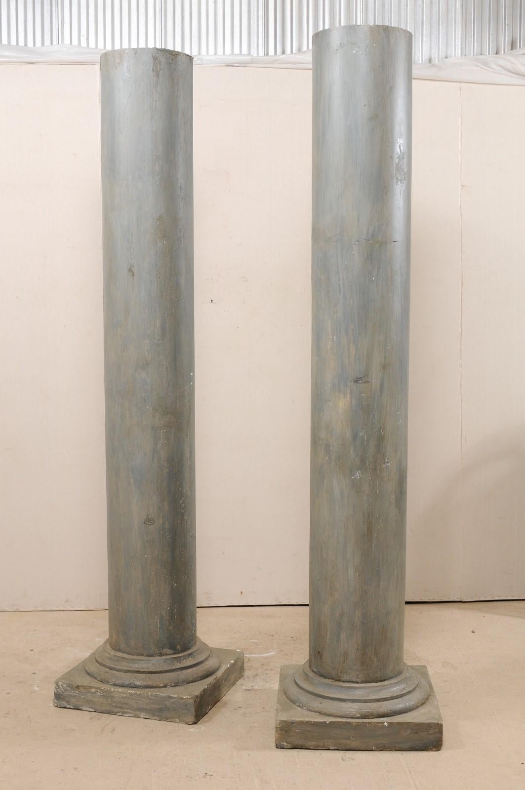 A tall pair of French painted plaster columns from the mid-20th century. These vintage Doric style columns from France feature rounded, straight, smooth shafts, and raised upon square bases. The columns have been painted in various shades of blue