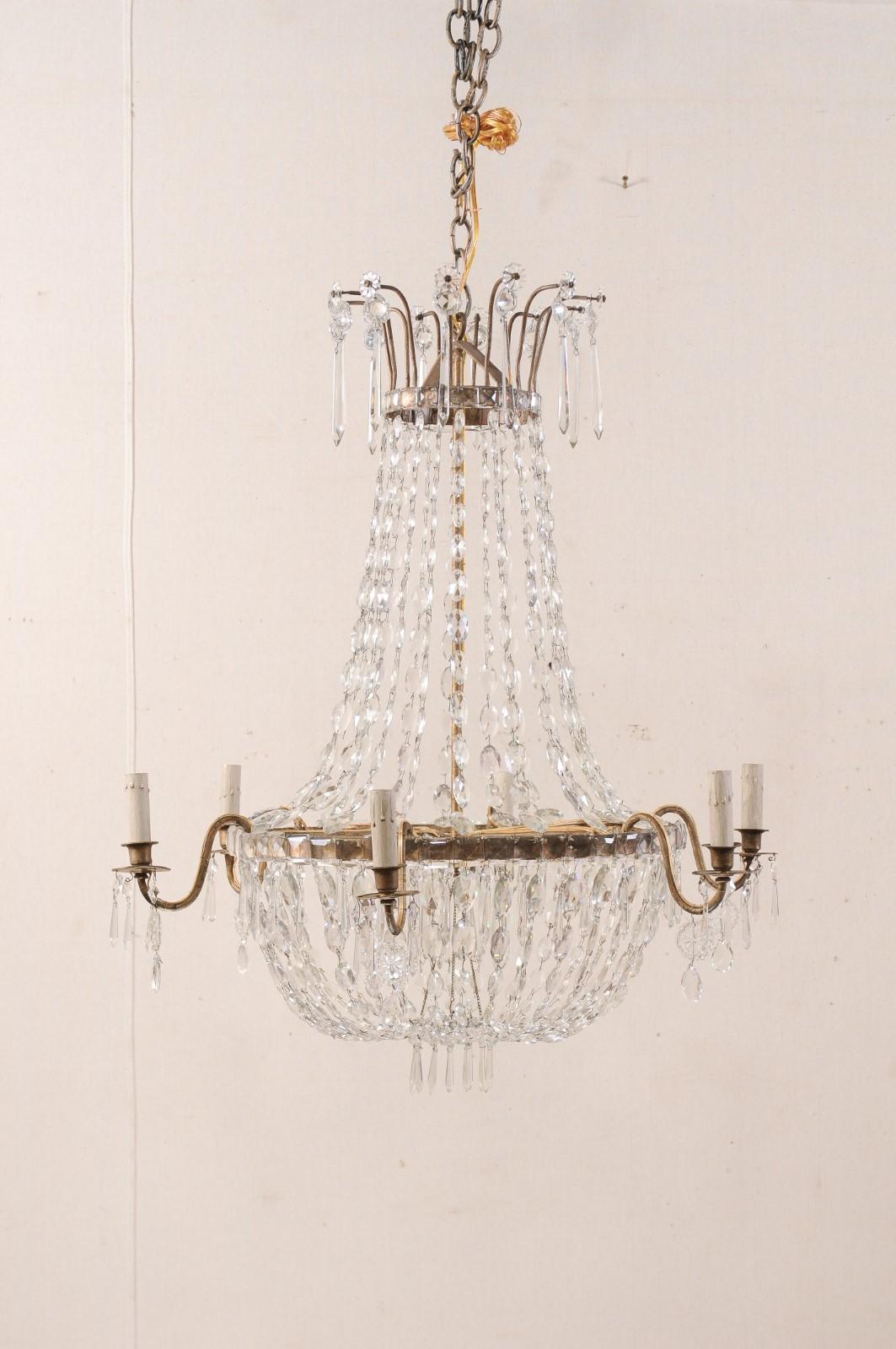 A pair of French Empire-style six-light chandeliers from the early to mid-20th century. These glorious chandeliers from France are each decorated in flowing strands of crystals, which swag down gracefully from the upper canopy, then drape from their