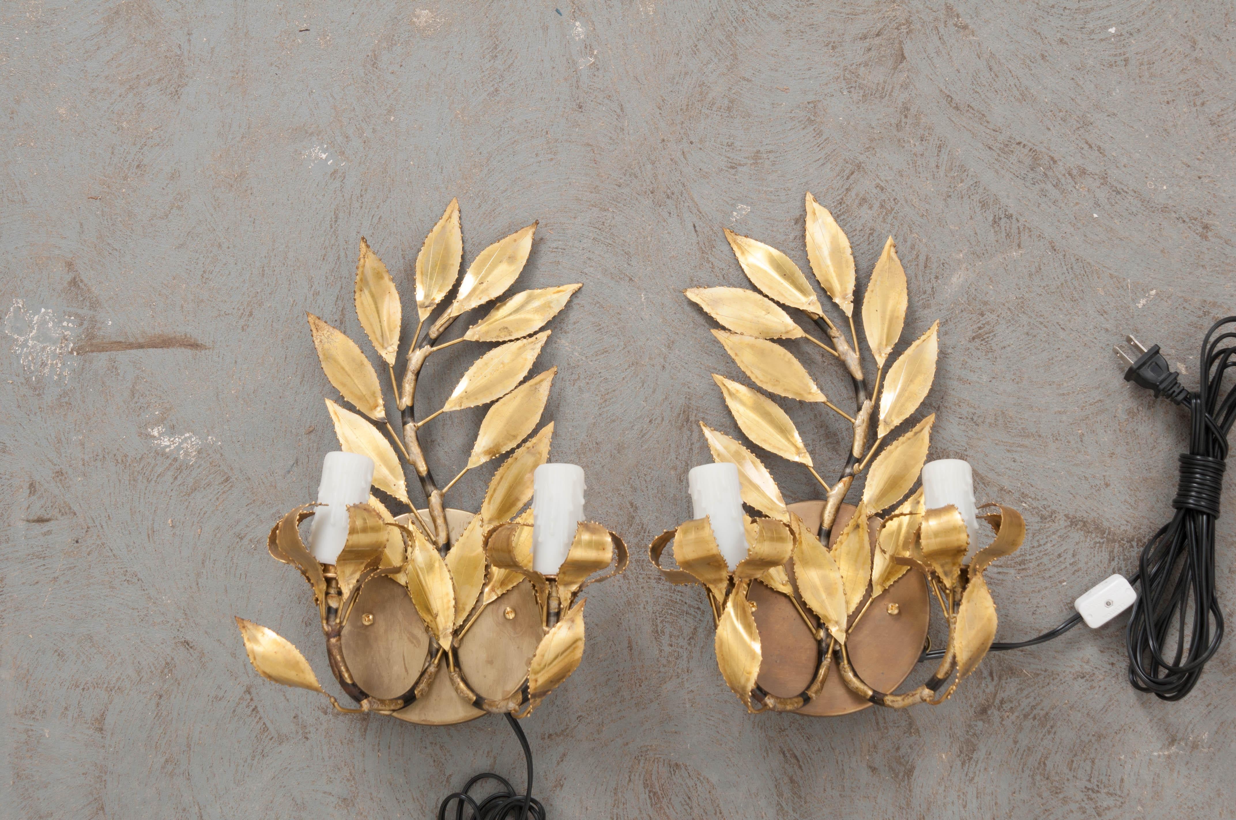 A fabulous pair of French vintage gilt-brass “laurel leaf” two-light sconces, circa 1970s, each light fashioned to appear as if sitting upon a melted candlestick.