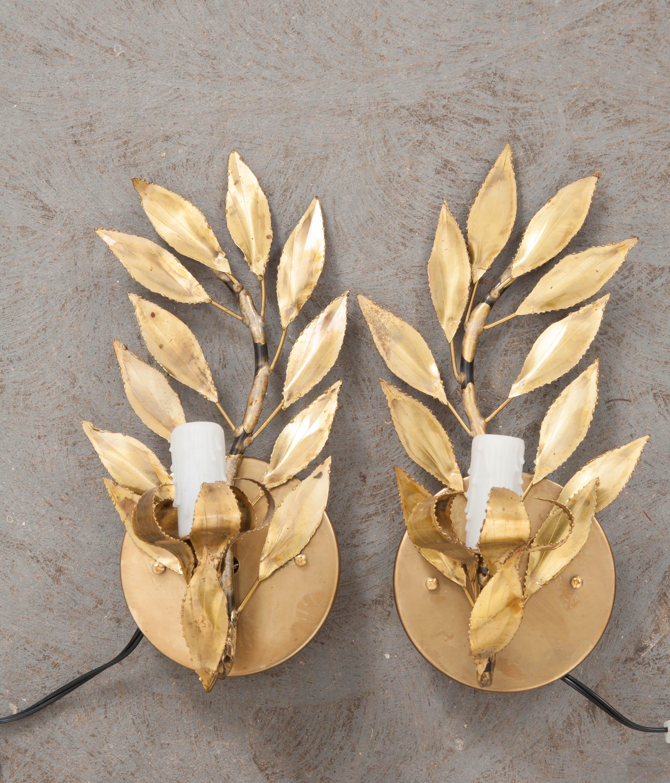 A fabulous pair of French vintage gilt-brass “laurel leaf” single-arm sconces, circa 1970s, each light fashioned to appear as if sitting upon a melted candlestick.
