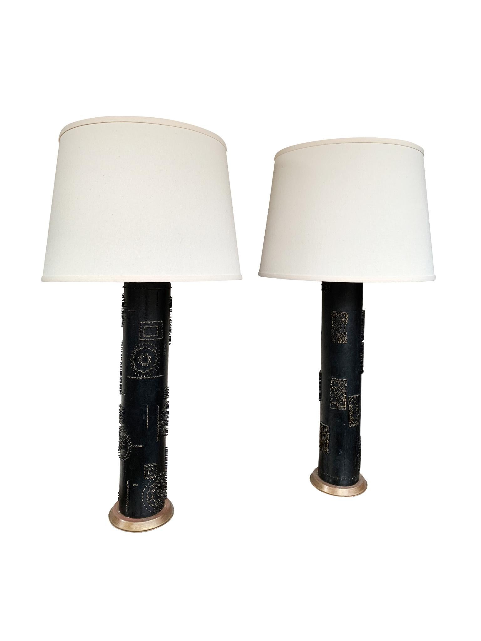 A beautiful pair of table lamps comprising of bases made from converted antique wallpaper rollers. They are black-painted wood with bronze-toned metal appliqué decorations and gold-hued round bases. The hardware is brass with double bulb sockets,