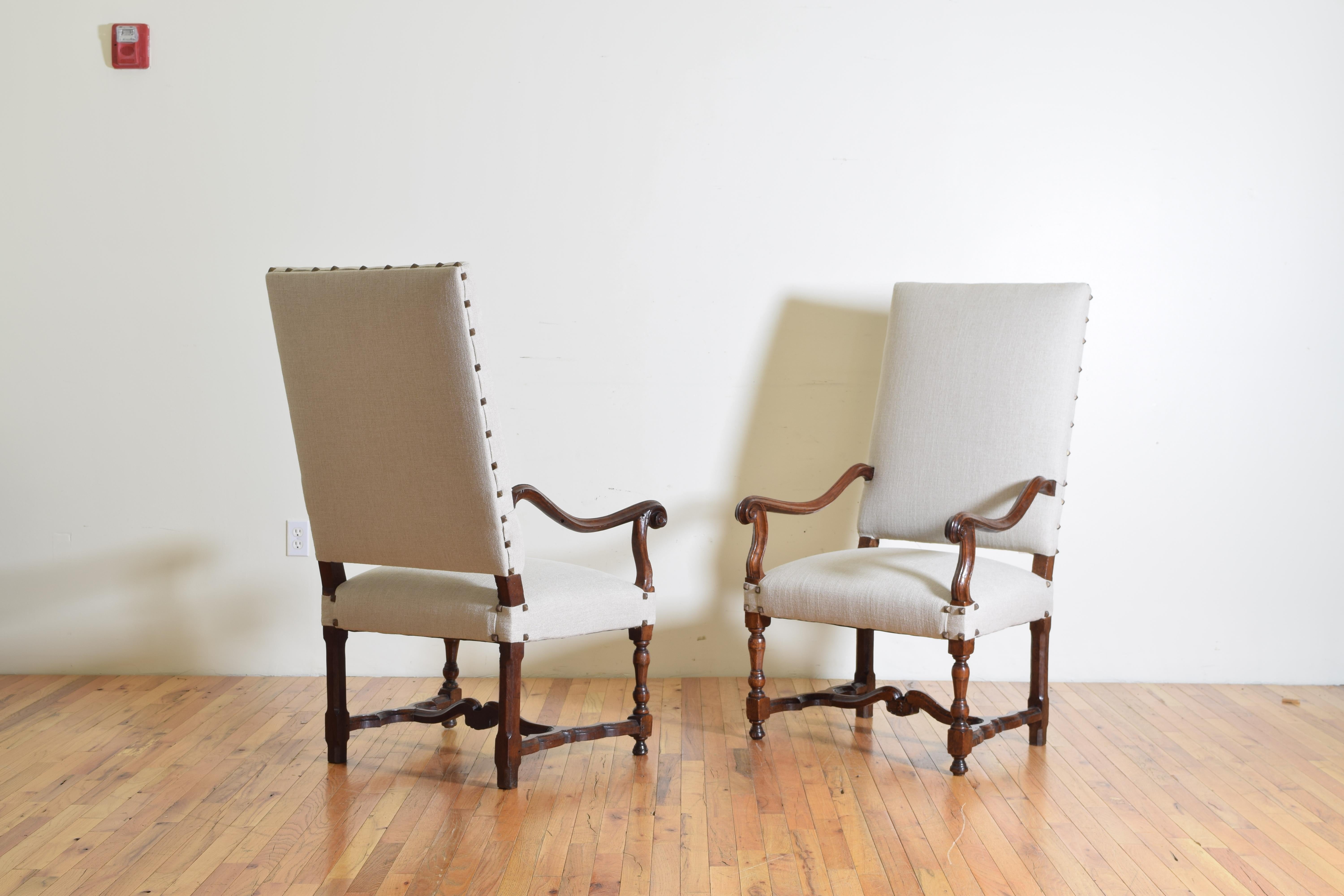 Newly upholstered in a beige linen and incorporating a melange of elements of 18th century periods these chairs have curved arms and arm supports, tight seats, and are raised on turned legs joined by curved stretchers.
