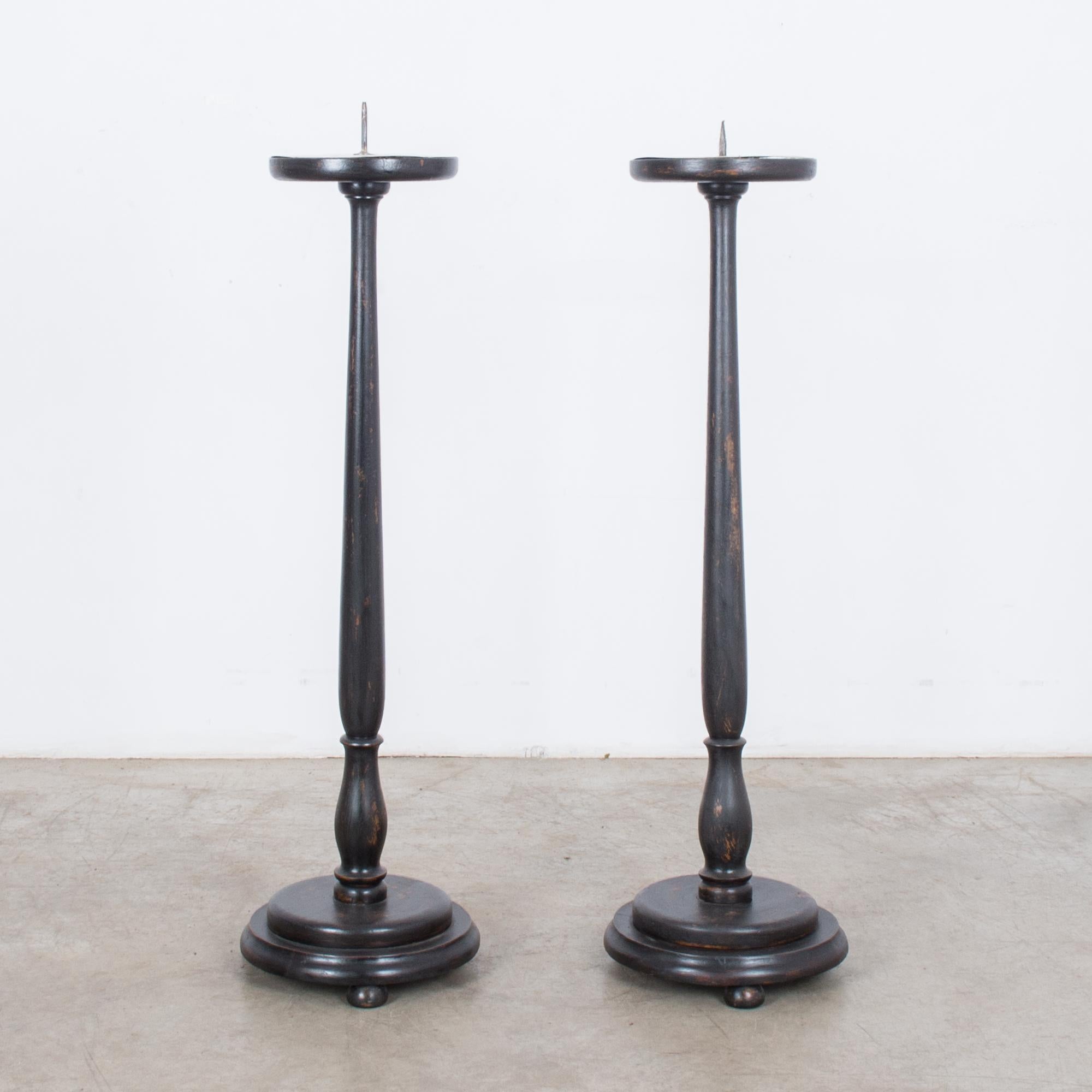 This pair of wooden candlesticks was made in France, circa 1900. Beautifully aged with a dark patina, the candlesticks have a circular drip pan with a pricket and a slim, baluster-style stem, which rests on a round and slightly elevated stepped base.