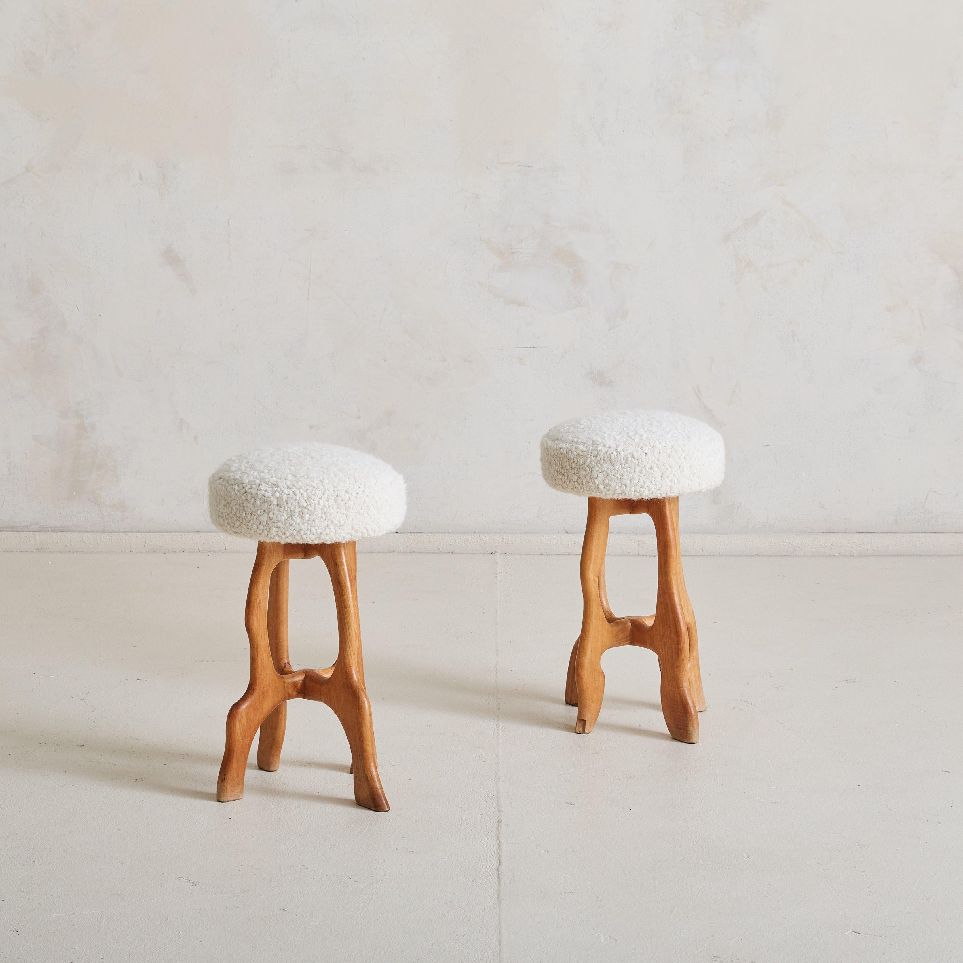 Una coppia scultorea di sgabelli francesi degli anni '60, reimmaginati con un'imbottitura in peluche color crema. Le basi in legno naturale sono caratterizzate da curve aggraziate e gambe affusolate che conferiscono un'atmosfera organica e