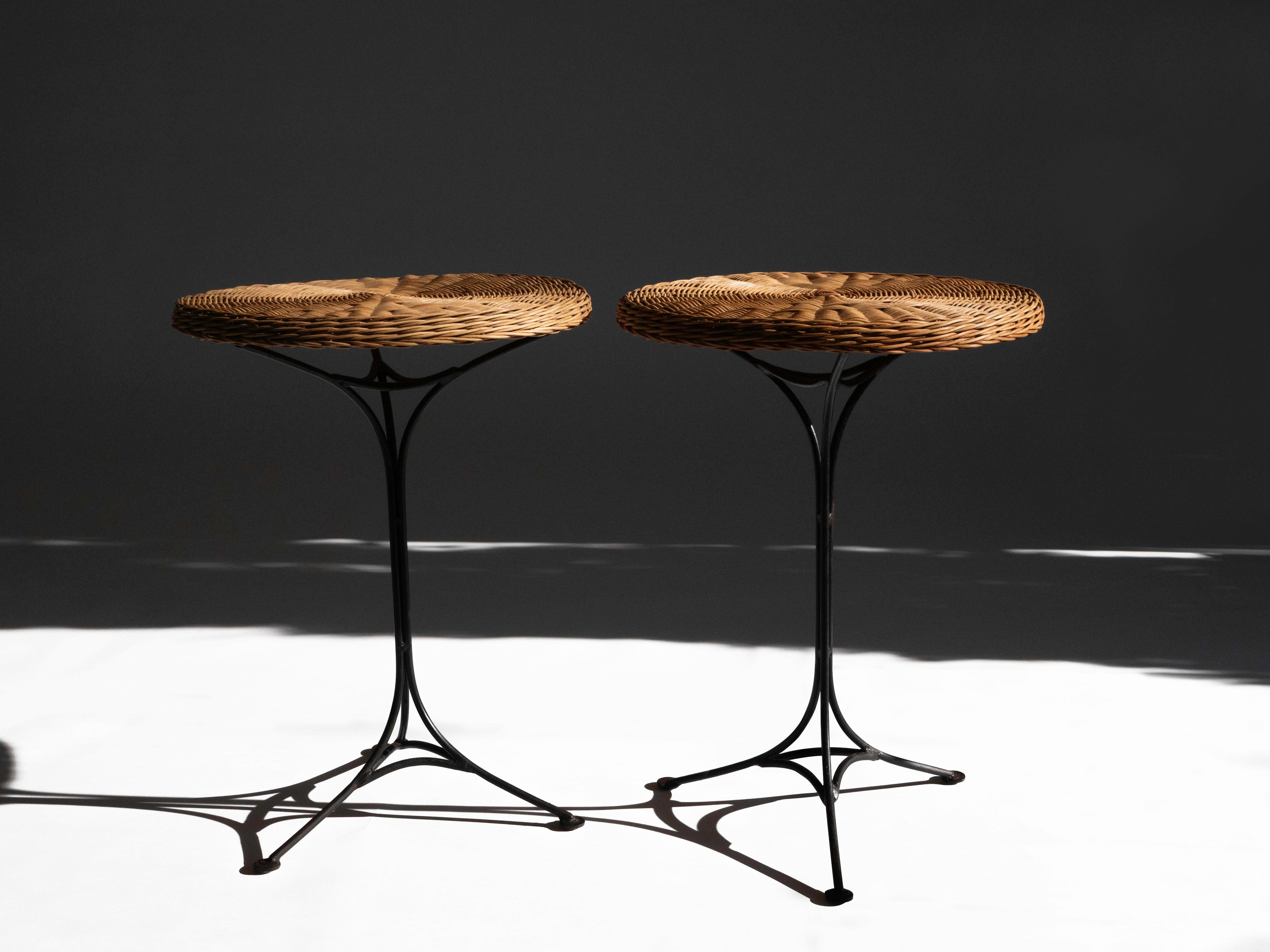 Paire de tables d'appoint en rotin et en osier, avec plateaux tressés et bases en fer forgé, fabriquées en France vers les années 1950. Les bases sont fabriquées de manière experte avec une silhouette rappelant celle de la Tour Eiffel. 

Les deux