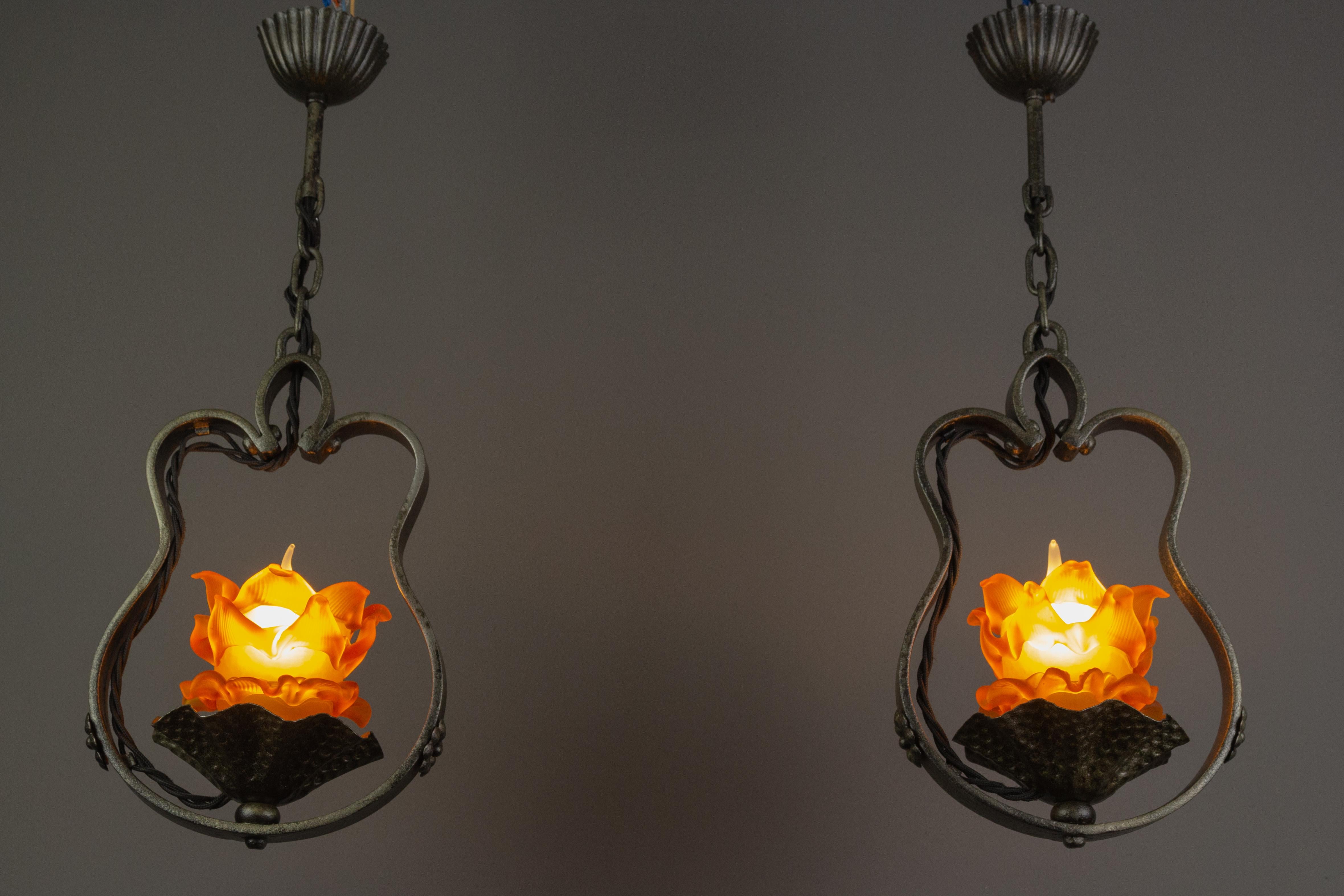 A nice decorative pair of French wrought iron pendant light fixtures in the shape of a water lily. Each light fixture has one beautiful flower-shaped orange or amber color glass paste lampshade and one socket for an E14 size light bulb.
Dimensions