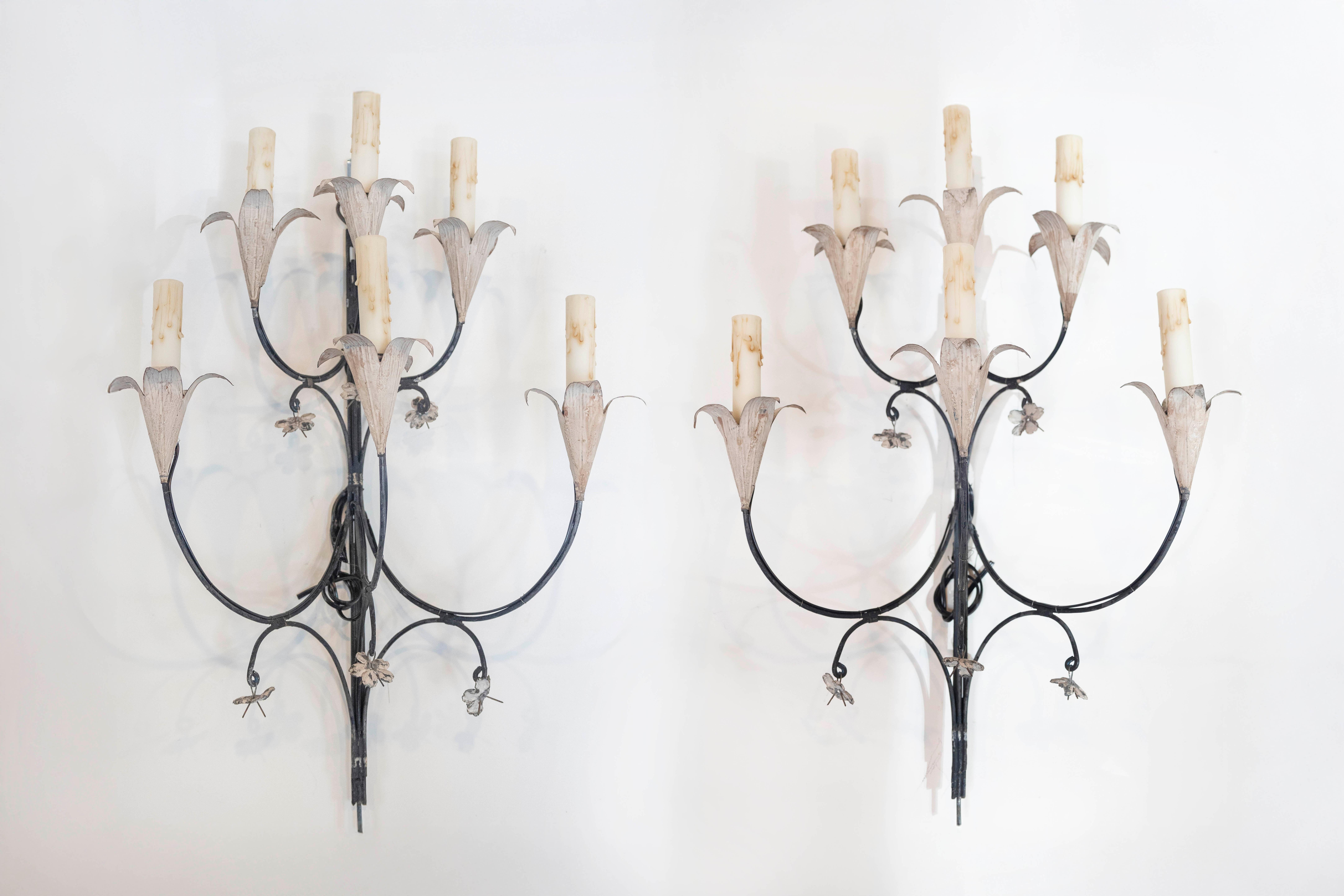 Une étonnante paire d'appliques françaises à cinq lumières datant des années 1940, magnifiquement fabriquées en fer forgé avec de délicats détails floraux en tole. Ces élégants luminaires muraux présentent des bras gracieusement incurvés, ornés de