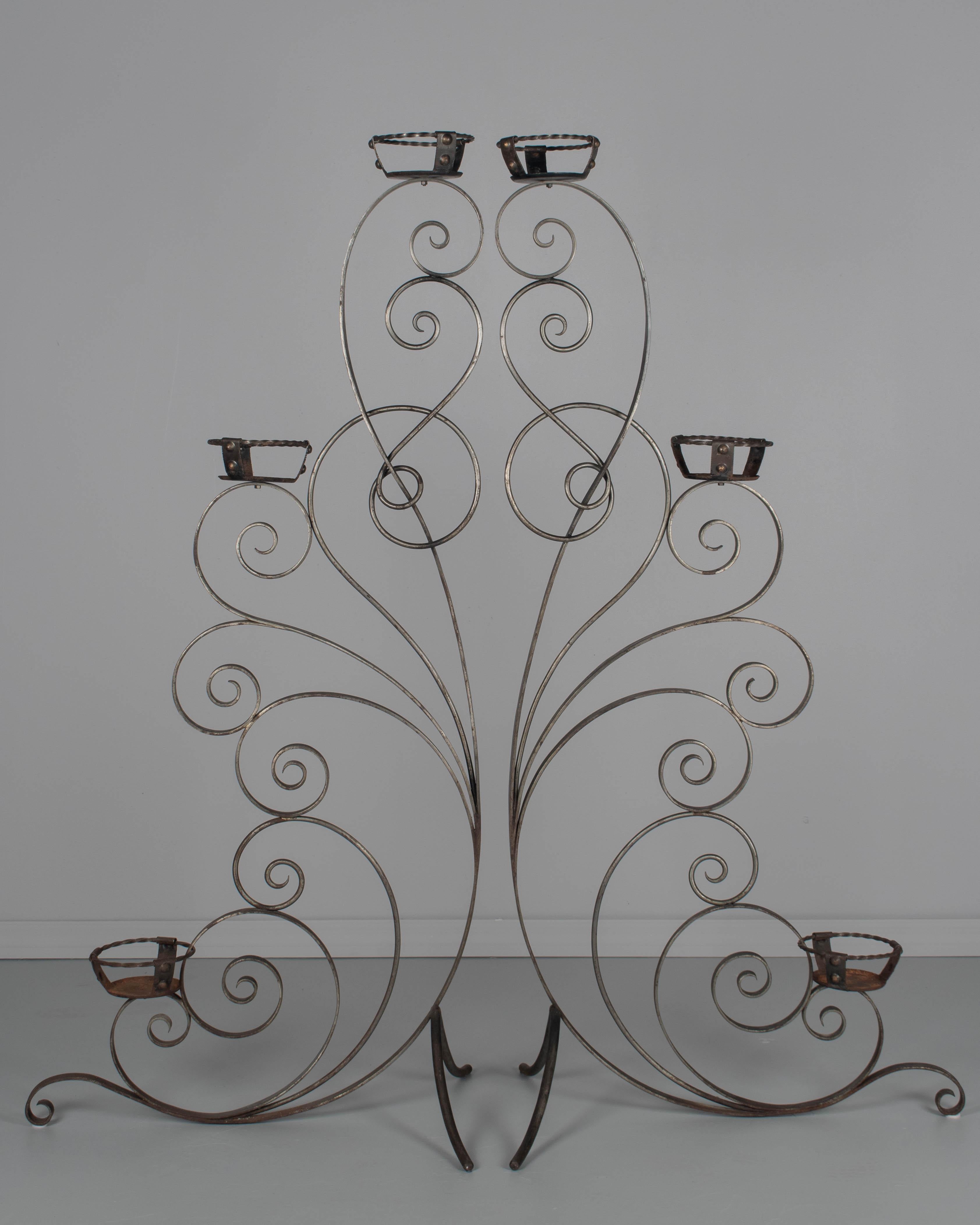 A pair of Vintage French wrought iron plants stands. Heavy, free-standing frames with good quality scrolled iron work. Each stand hold three plants, or may be used with pillar candles. In good condition with one break in welded element, some light