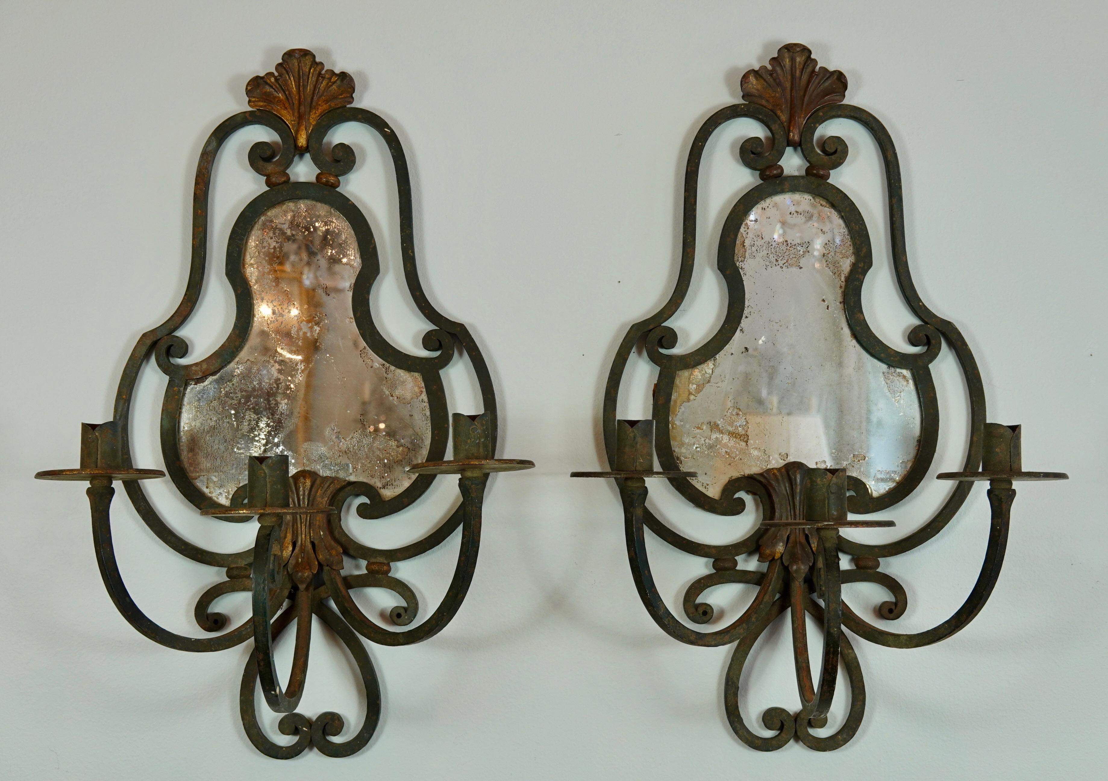 Large and impressive pair of French provincial wrought iron sconces with three arms and mirrored backs, (late 19th-early 20th century). Gilded tole acanthus leaf details. Two pairs are available. One pair (see photos), features old mercury glass