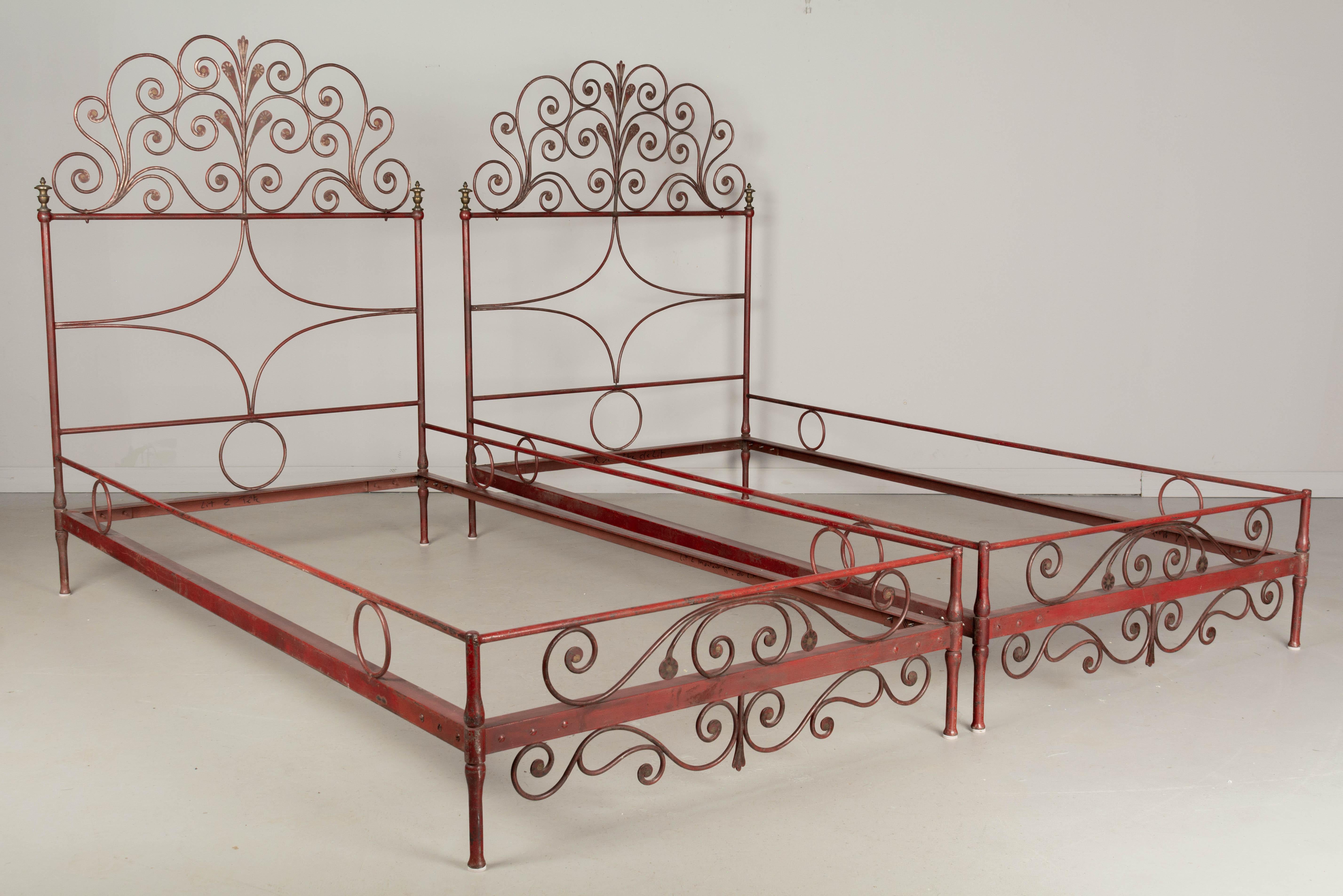 A pair of French Napoleon III style iron bed frames with original red painted finish. Decorative wrought iron headboard and footboard accented with gold painted floral details. Cast brass finials. Minor paint loss. In good condition with nice