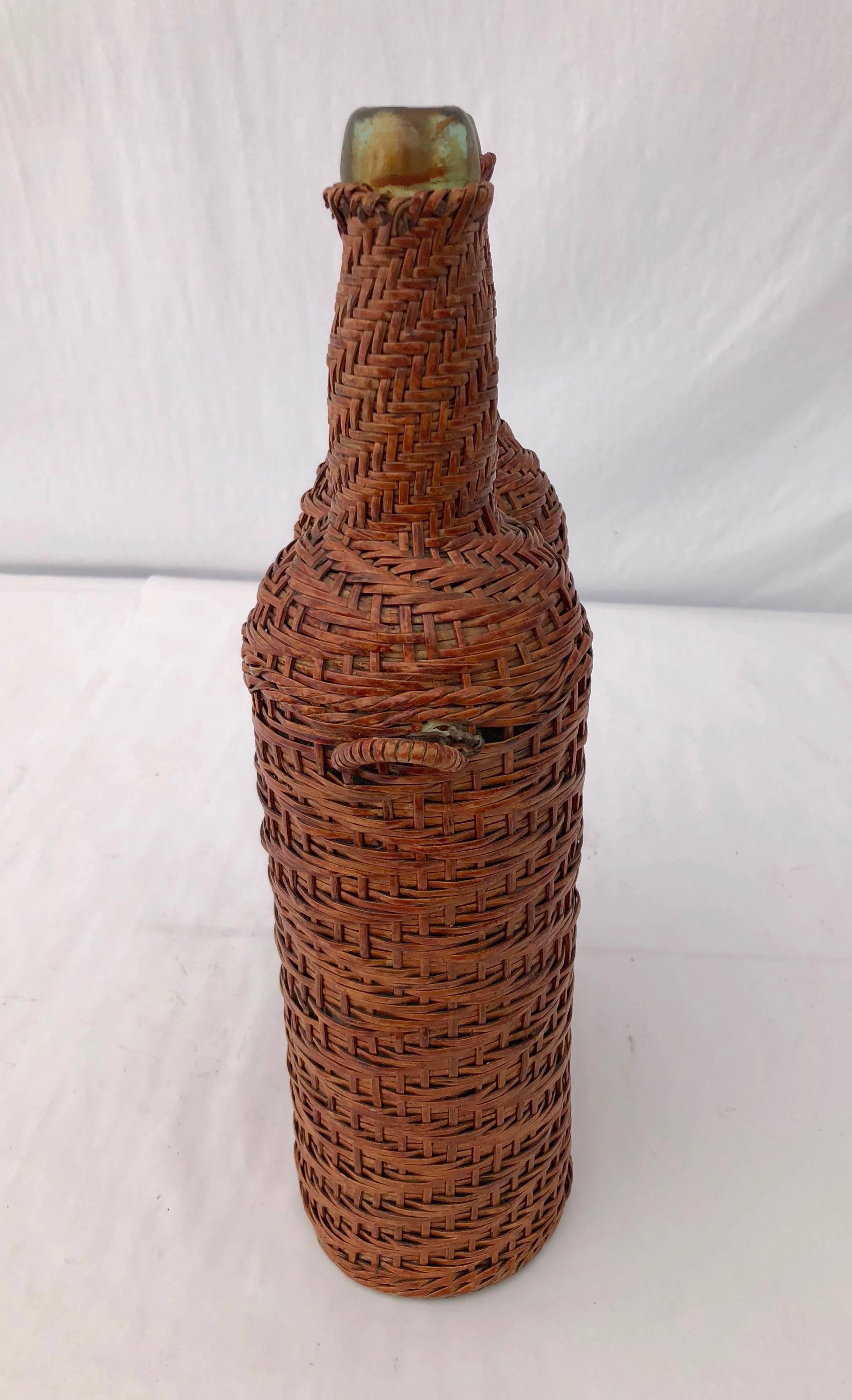 This is a great pair of French hand blown bottles in a greenish color glass covered by a light brown woven wicker. It comes with a detached handle. This would be great as an original vase for fresh cut lowers or as a decorative piece.