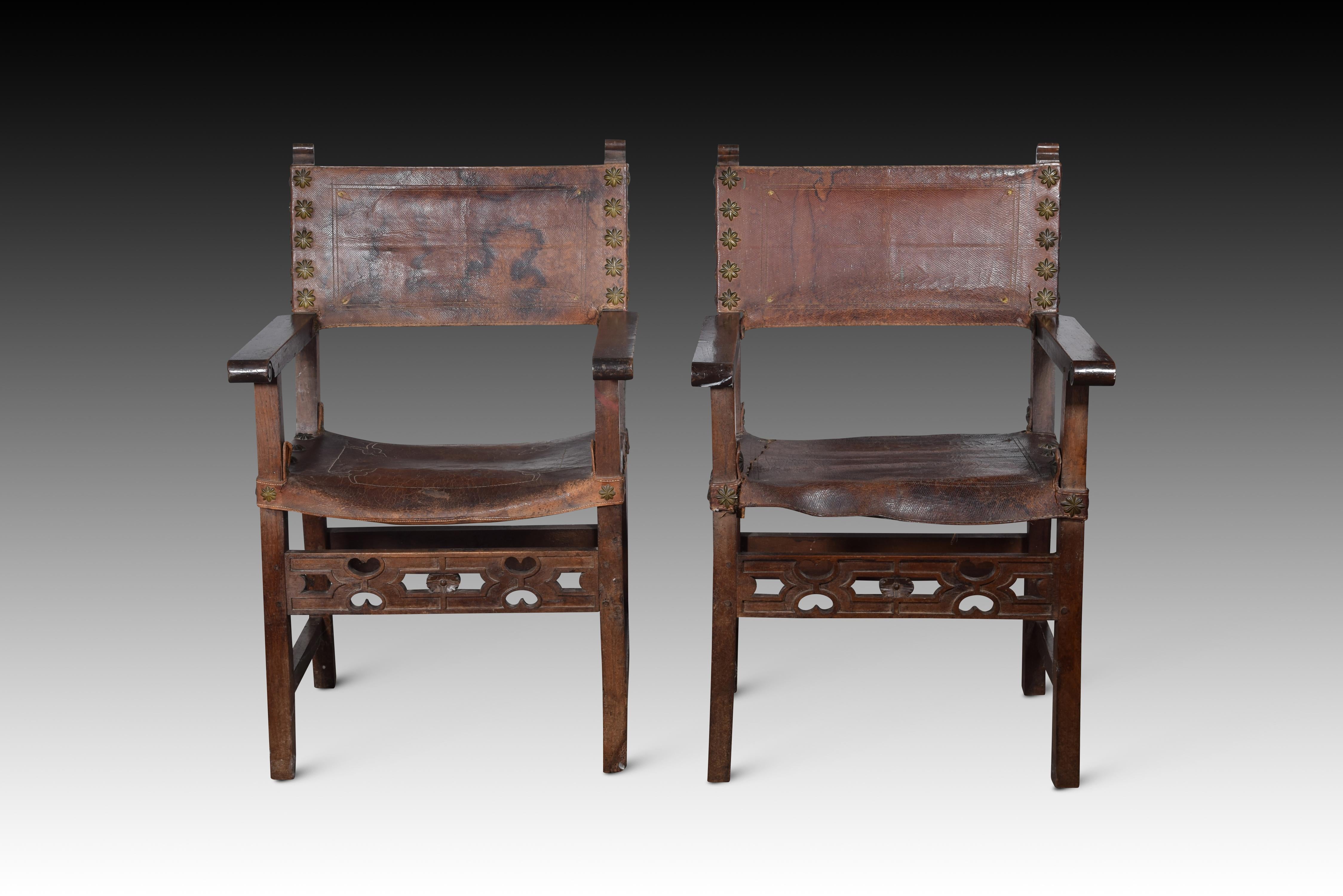 Pair of friar armchairs. Walnut wood, leather, metal. Spain, 17th century. 
Armchairs with arms and high backs of the type known as “frailero”, which have leather with studs on the seat and upper part of the back, low chambranas joining the front
