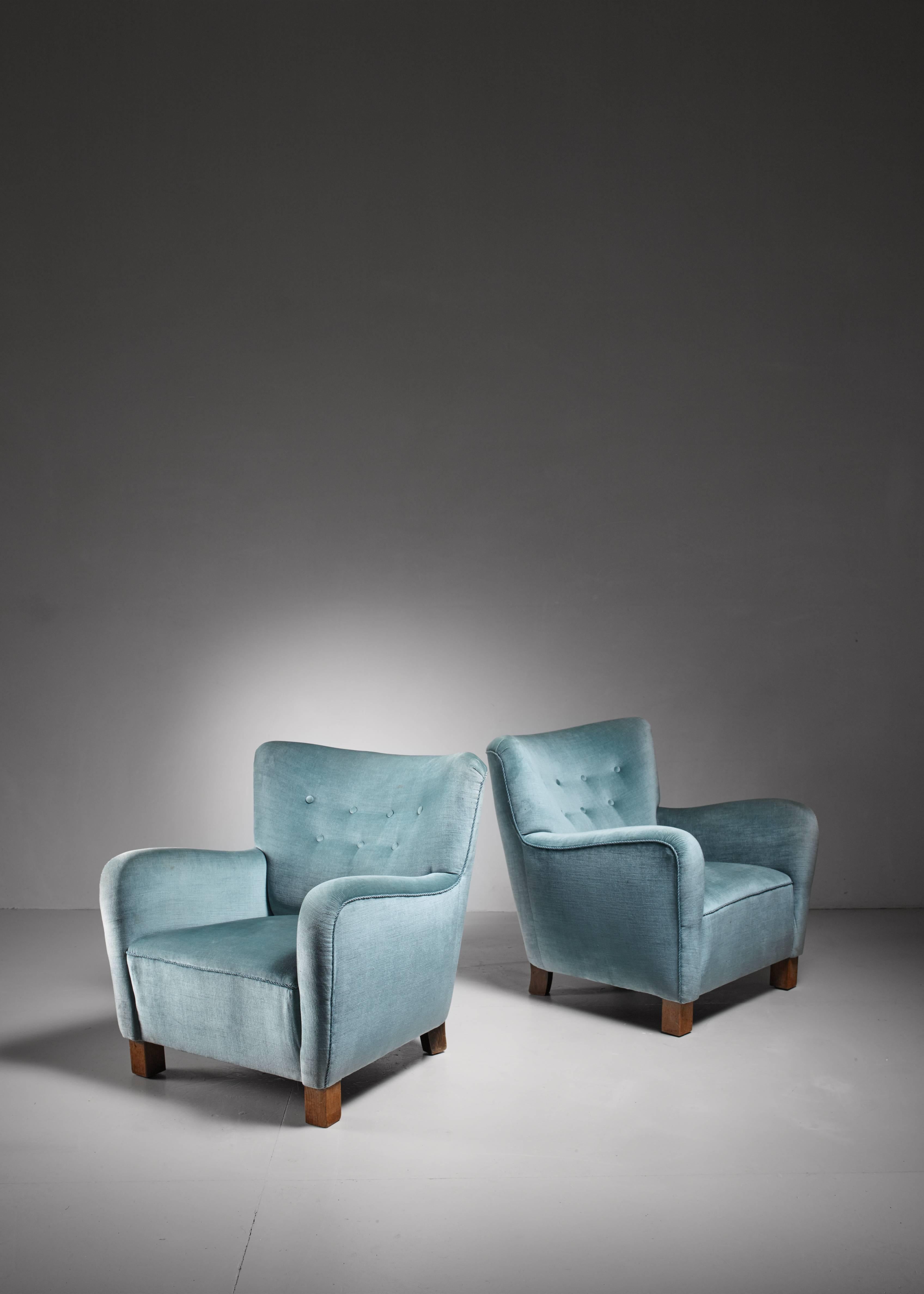 A pair of Danish lounge chairs with a blue, buttoned velvet upholstery. The chairs are a variation on model 1669 by Fritz Hansen. A wonderful and comfortable pair.