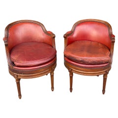 Pair of fruitwood swivel chairs in ox blood leather with Gouffe label