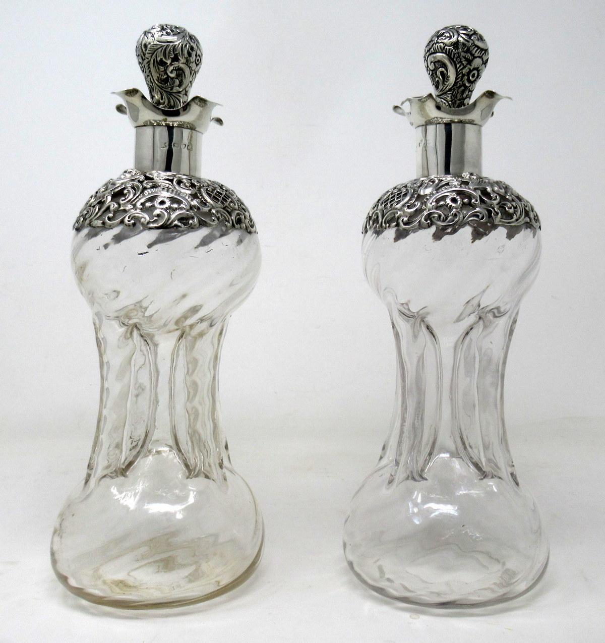 Stunning identical pair of English sterling silver mounted glass spirits or wine decanters of waisted form, late nineteenth century.

The unusual original silver covered ball formed glass stoppers above wavy shaped silver mounts and richly