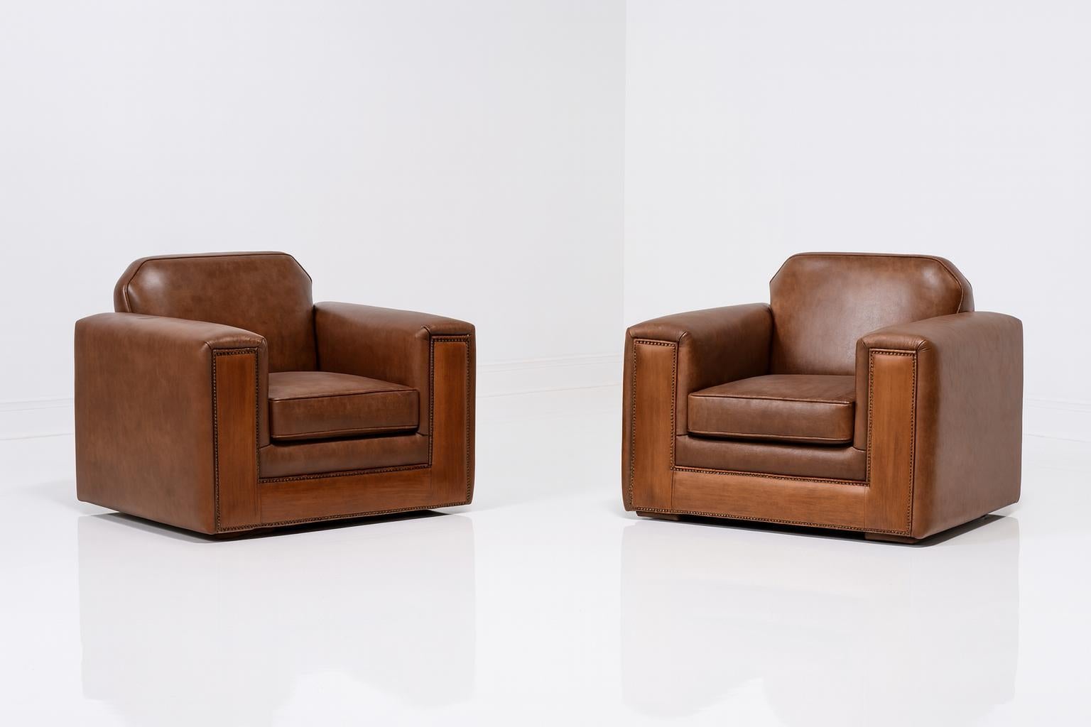 This pair of restored European Art Deco club chairs embodies strength, style, and sophistication. Fully restored from the frame up, these chairs feature a striking two-tone leather design that blends antique-distressed, waxed brown hides with a