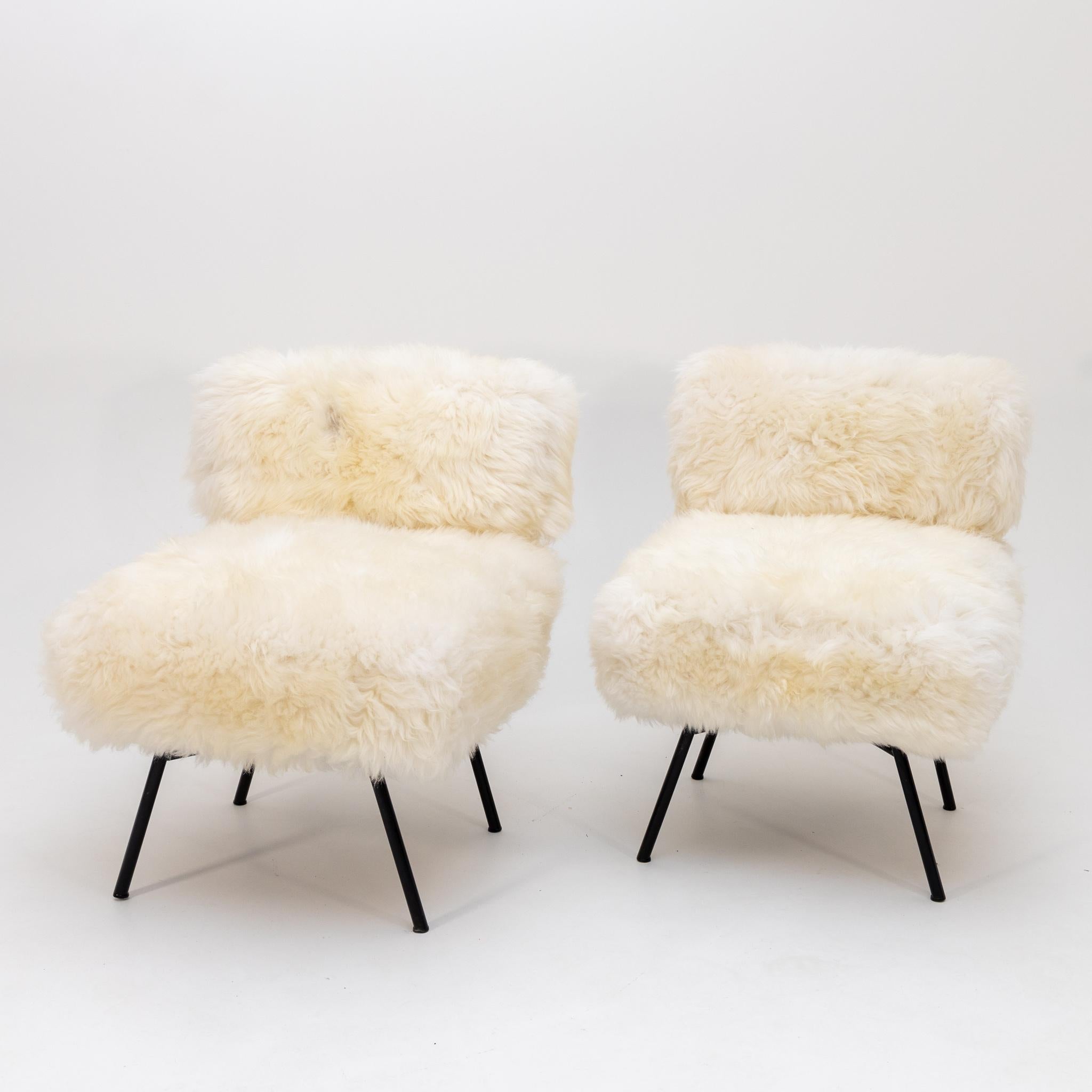 Pair of smaller lounge chairs on iron legs. The armchairs have been re-covered with sheepskin.