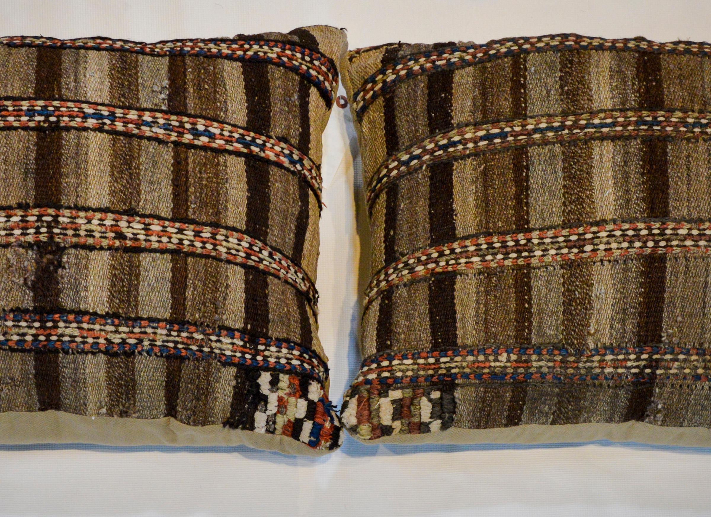 A pair of pillows made from an early 20th century Gabbeh kilim rug woven with natural brown and beiges wool, and with several crimson and indigo stripes crossing the face.